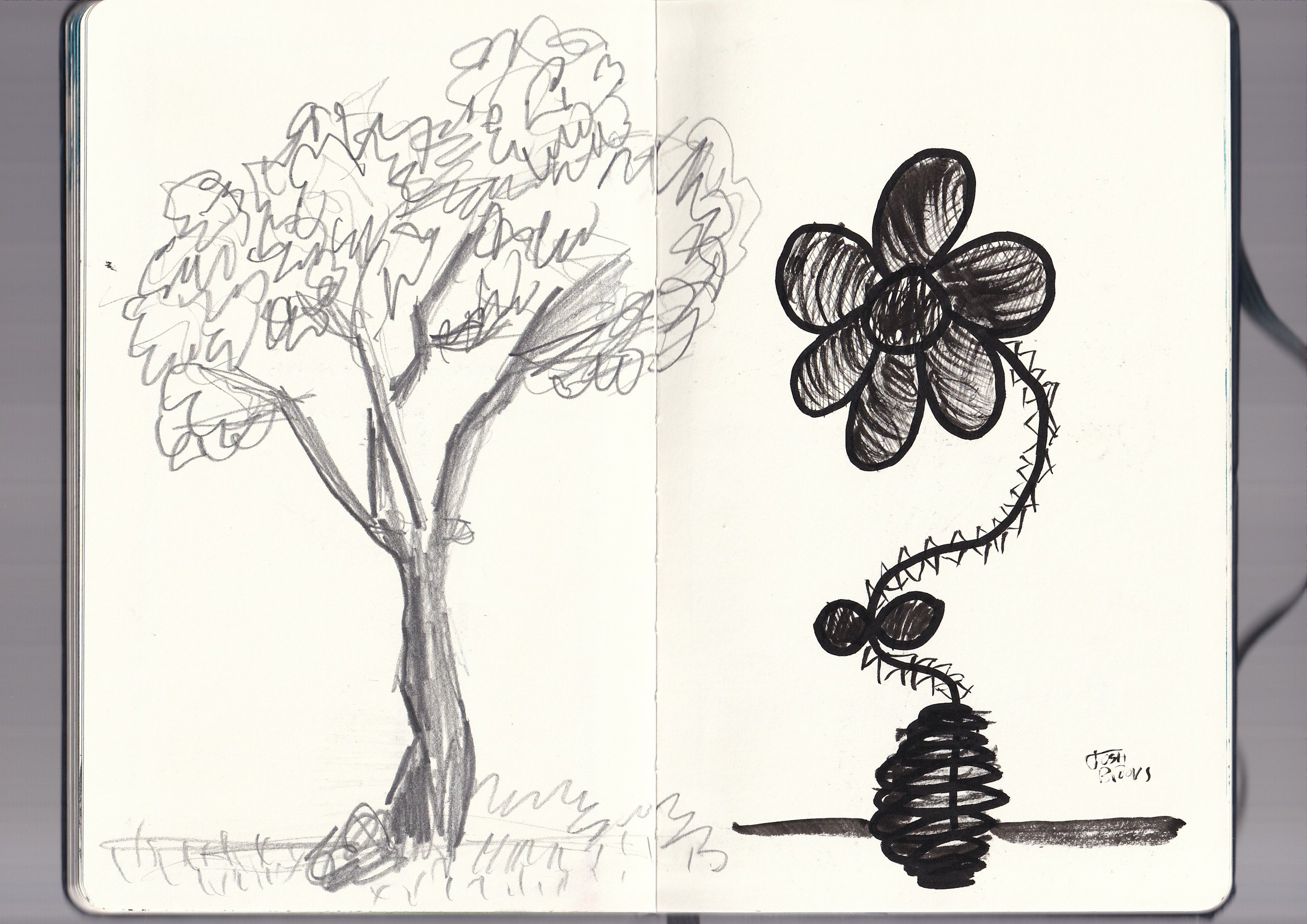 A sketchbook opened to reveal two sketches: on the left, a detailed pencil drawing of a tree with a thick trunk and numerous branches and leaves; on the right, a bold, black ink drawing of a flower with five petals and a coiled stem.