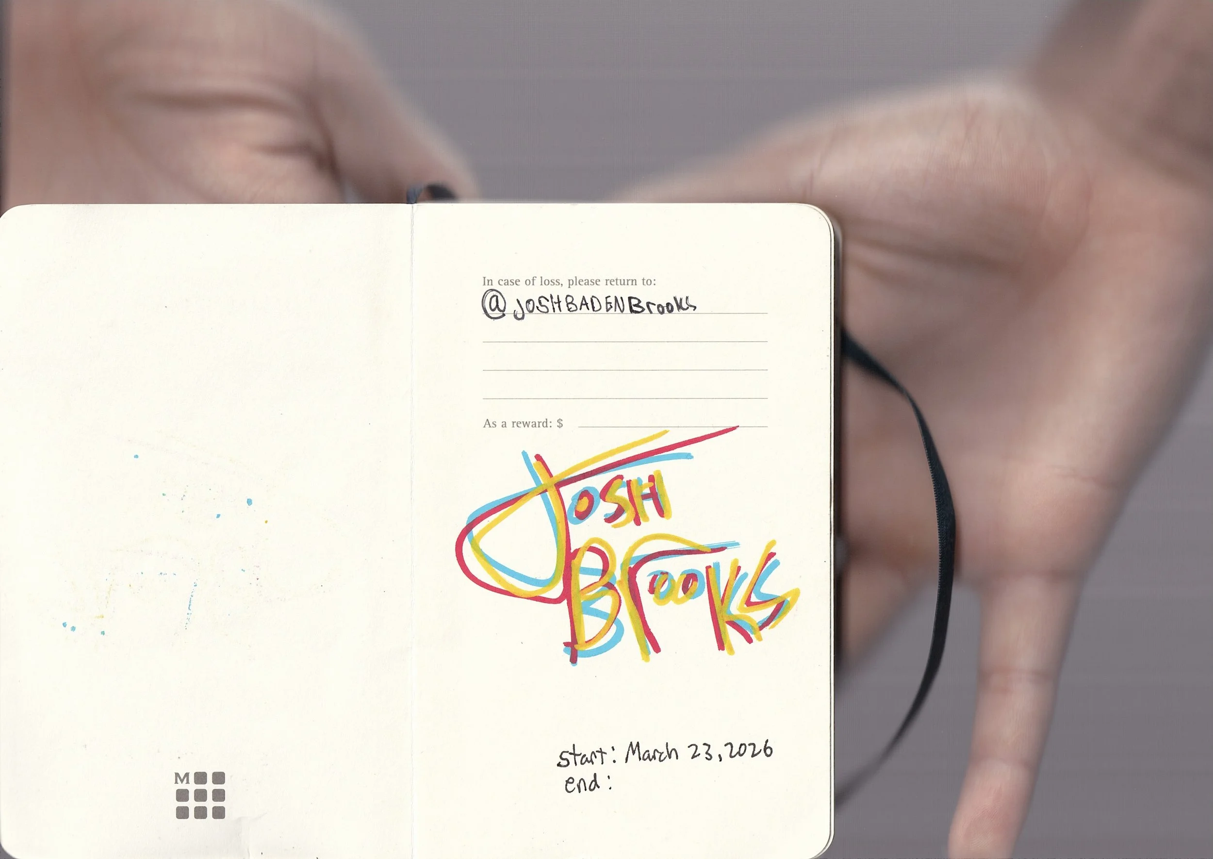 A close-up photograph of a person holding an open notebook with handwritten notes and colorful doodles on the right page. The left page is mostly blank. The person's fingers are visible on the right side of the image, and they are wearing a black bra
