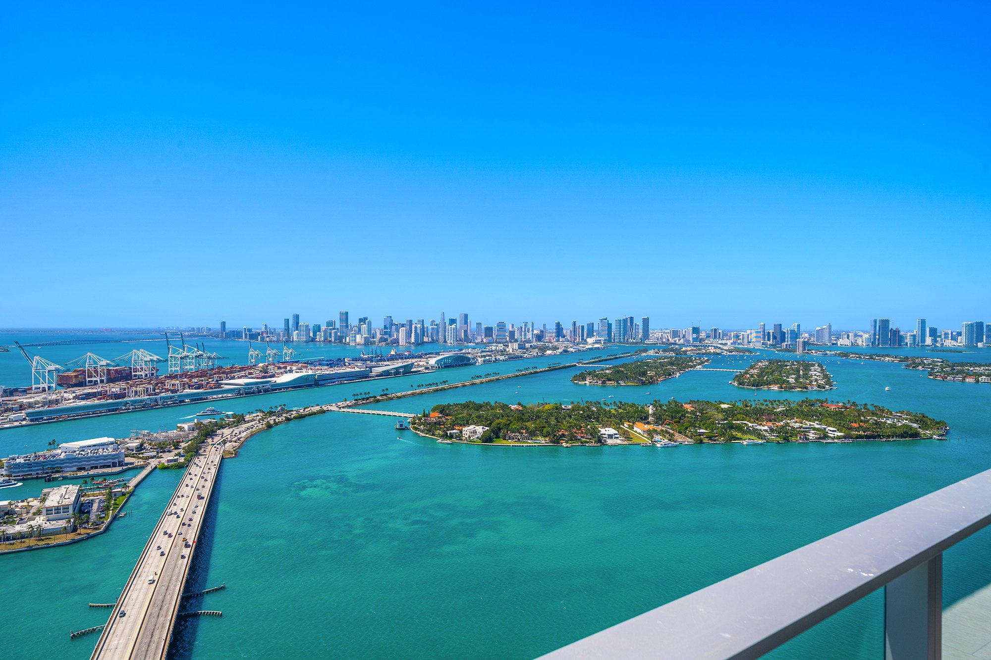 Aerial view of Miami skyline with cruise terminal, green water, and islands, under a clear blue sky.