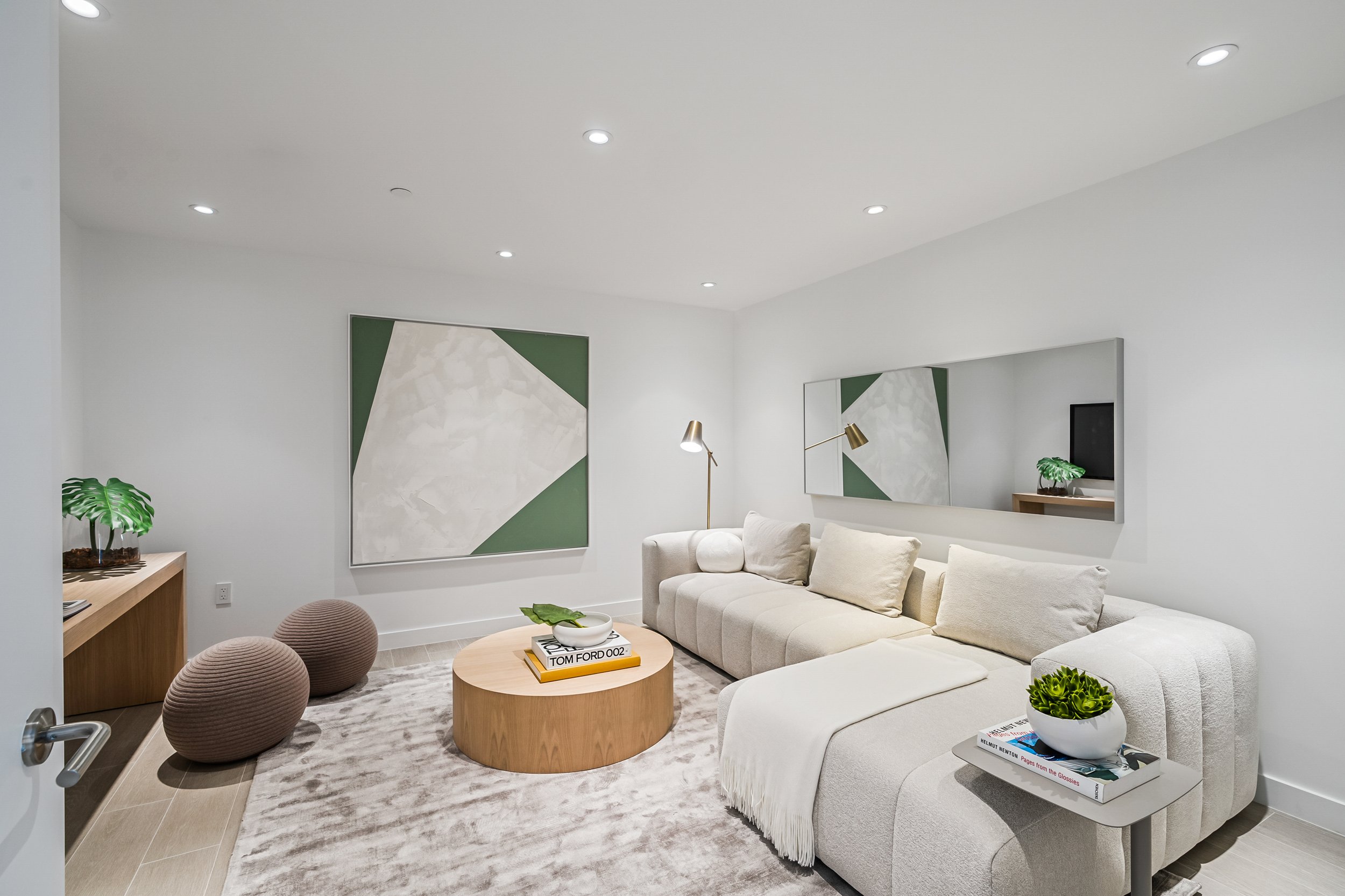 Modern living room with a white sectional sofa, round wooden coffee table, abstract wall art, and neutral decor.