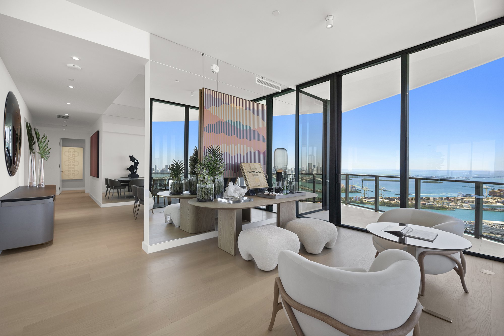 Modern luxury apartment interior with large windows offering a waterfront city view, featuring contemporary furniture, minimalist decor, and natural lighting.