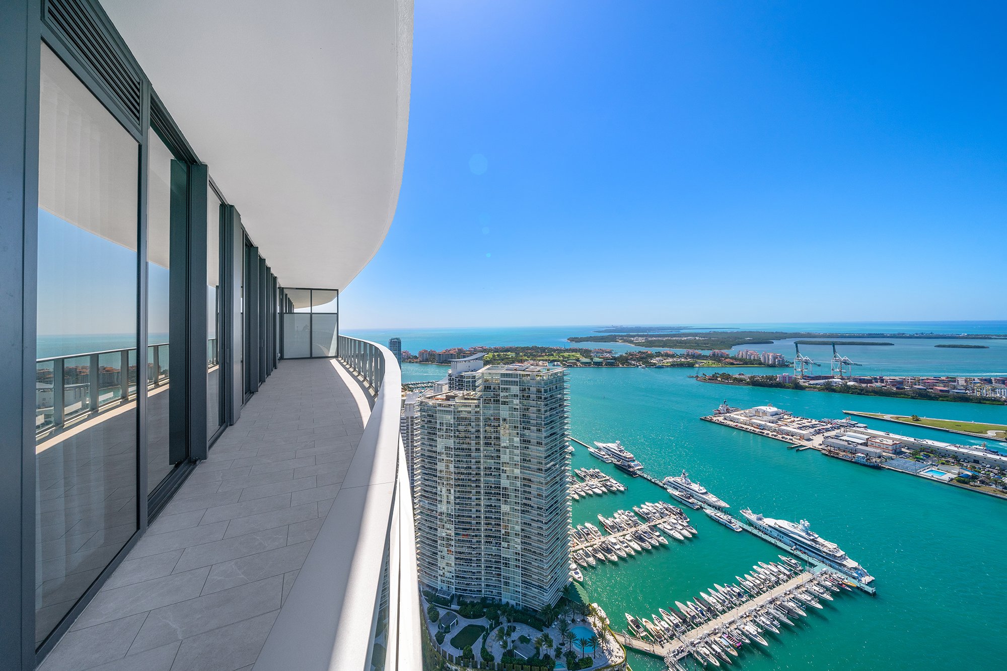 High-rise building balcony with ocean view, featuring yachts in a marina and distant islands under a clear blue sky.
