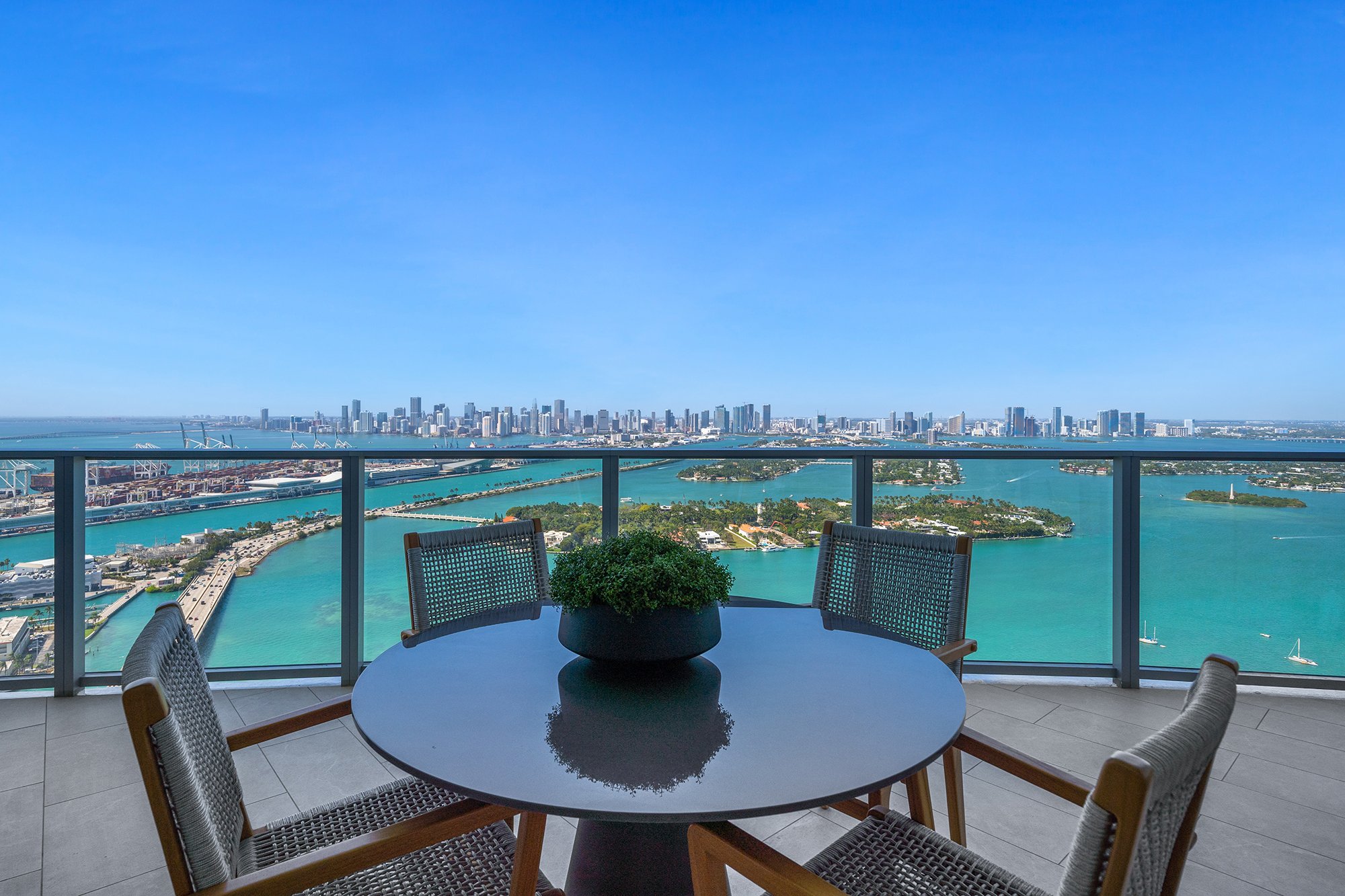 Outdoor balcony with table and chairs overlooking city skyline and ocean.
