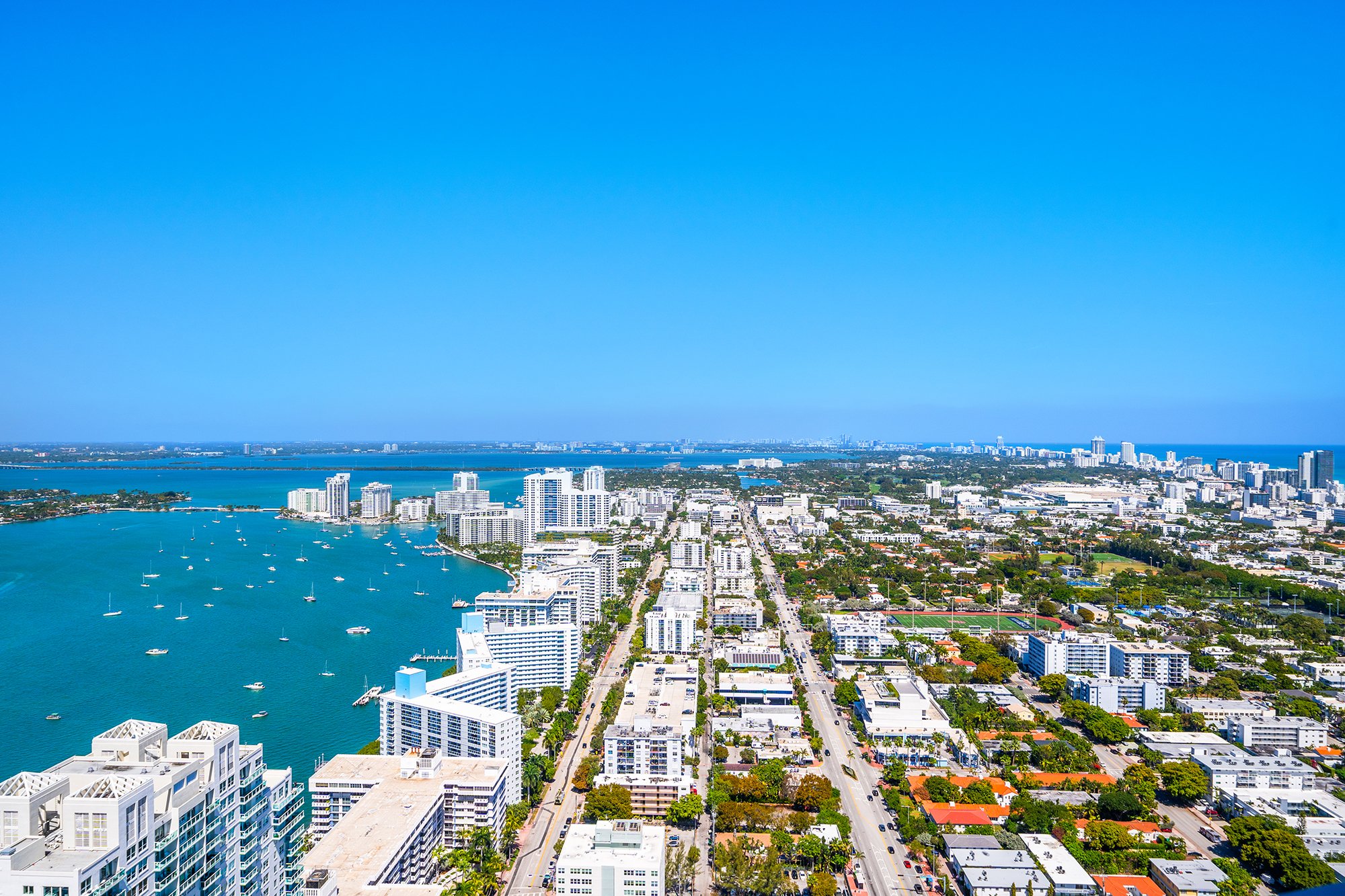 Aerial view of Miami Beach with turquoise waterfront, high-rise buildings, and tree-lined streets on a clear day.