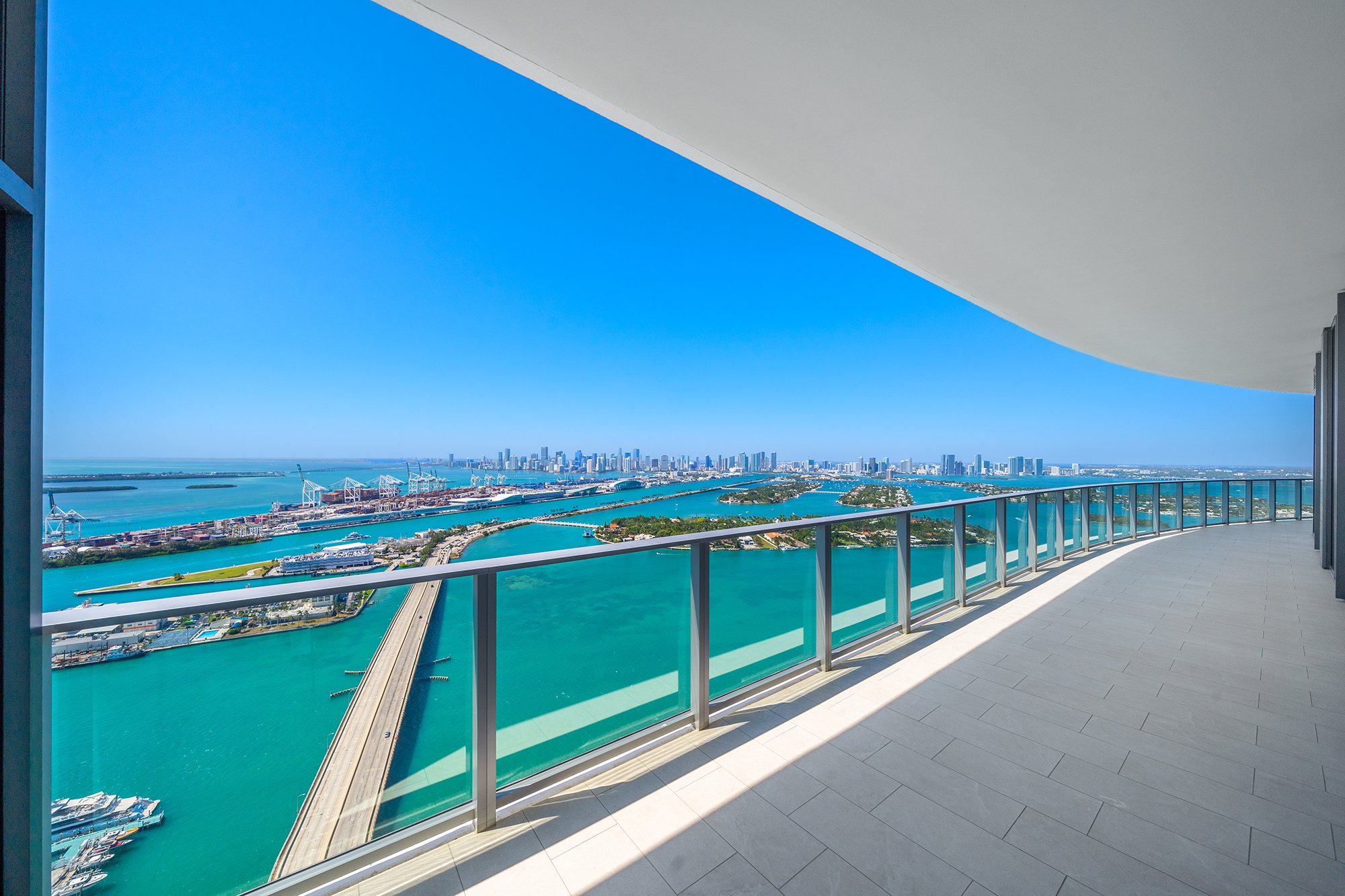 High-rise balcony view of ocean, city skyline, and islands against a clear blue sky.