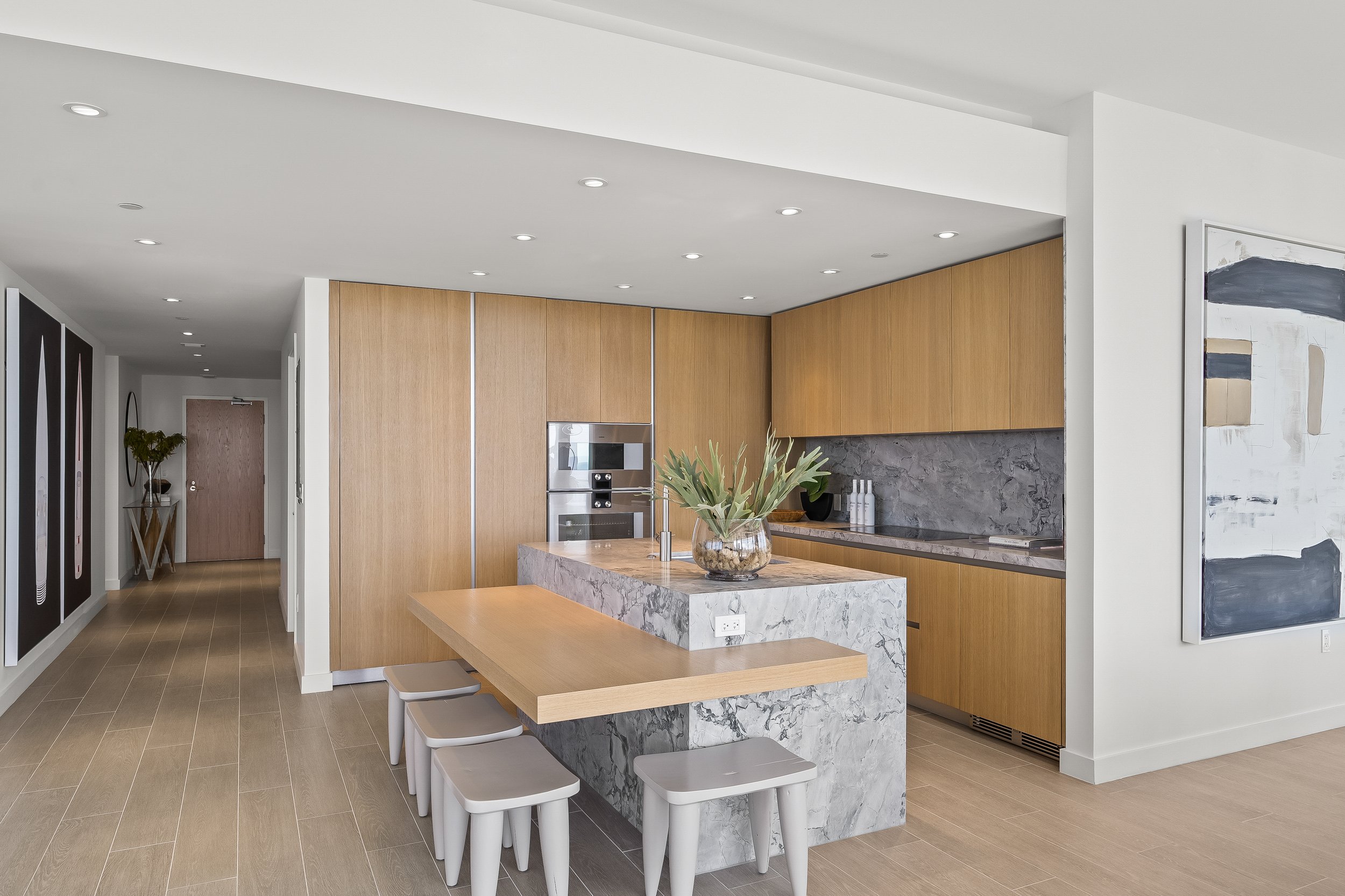 Modern kitchen with marble island, wood cabinets, built-in appliances, and barstools.