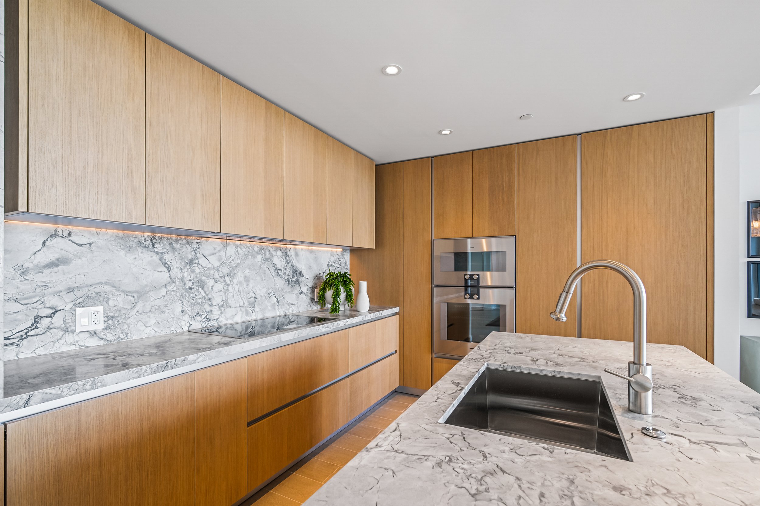 Modern kitchen with wooden cabinets, marble countertops, stainless steel appliances, and a sleek faucet.