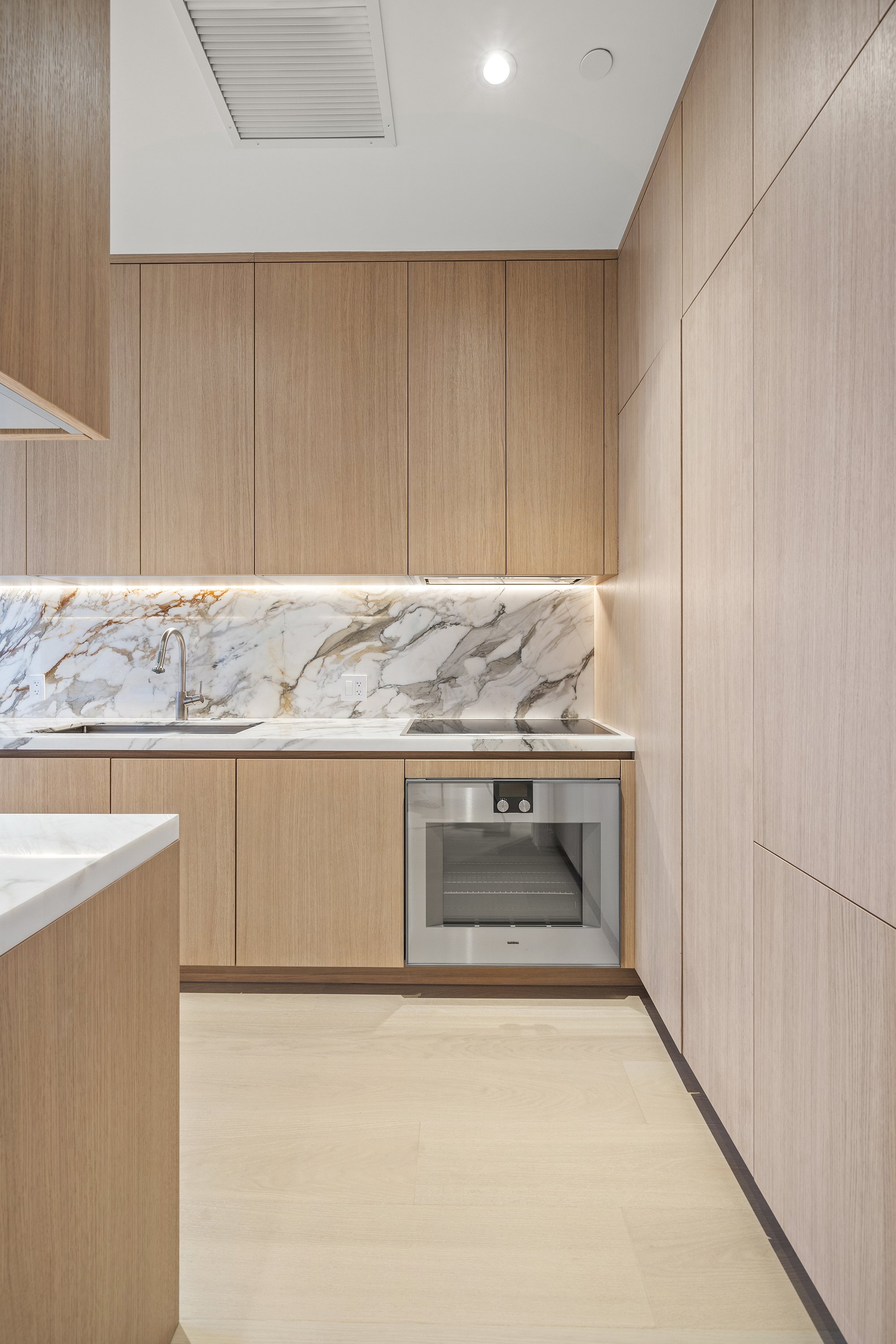 Modern kitchen with wood cabinetry, marble backsplash, built-in oven, and minimalist design.
