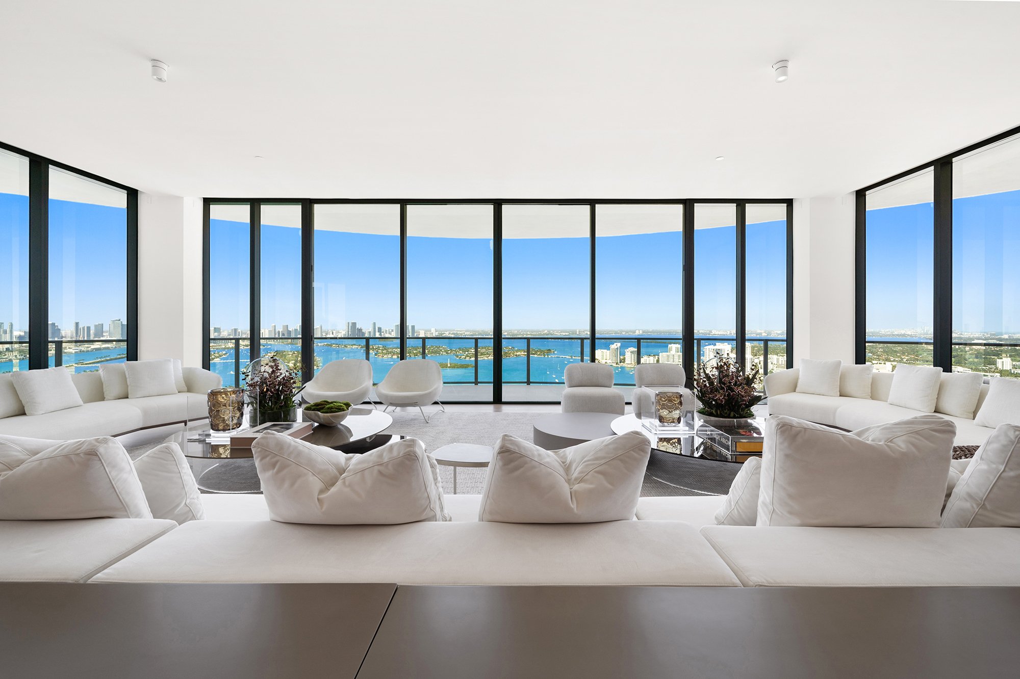 Modern living room with white sofas, large windows, and city skyline view.