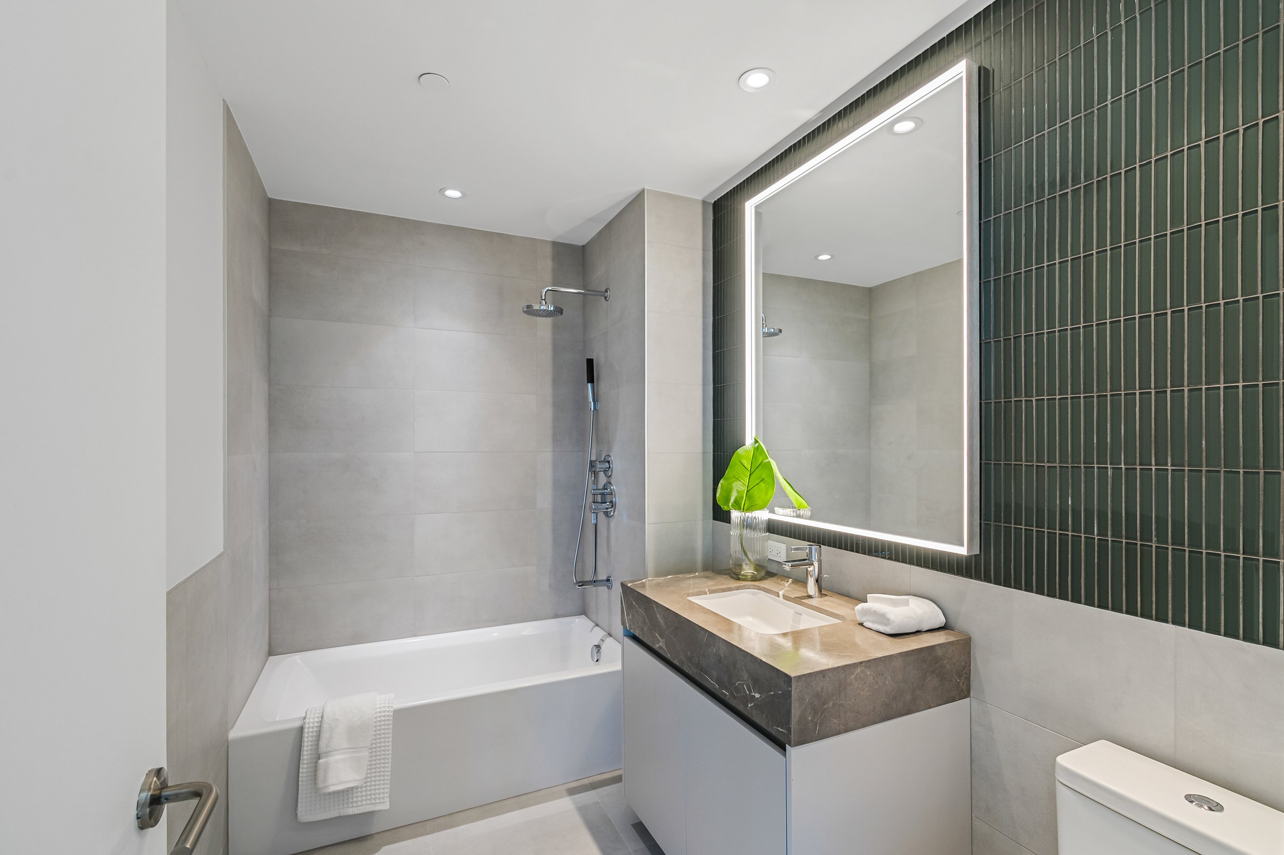Modern bathroom with a bathtub, shower, large mirror, sink, and green tiled wall.