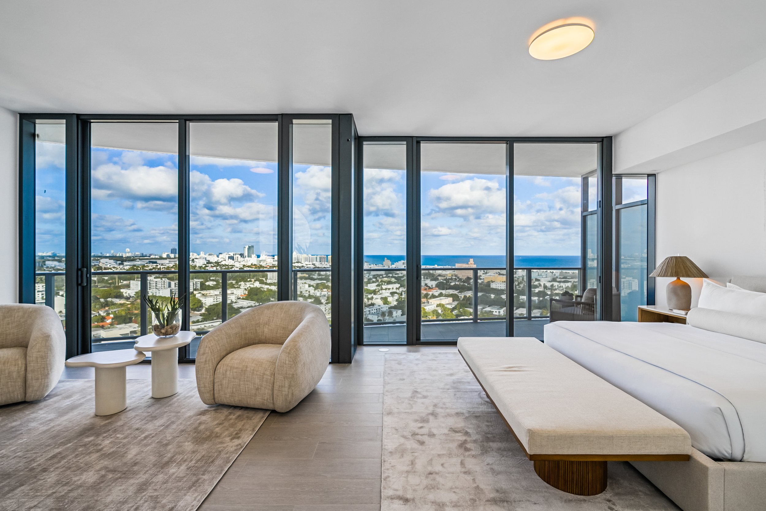 Luxury bedroom interior with panoramic city and ocean view, modern furniture, and floor-to-ceiling windows.