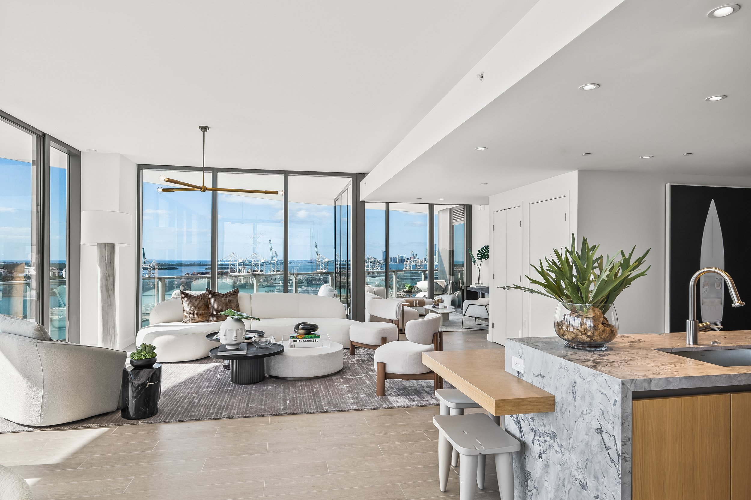 Modern living room with ocean view, white sofas, marble kitchen island, and sleek decor.