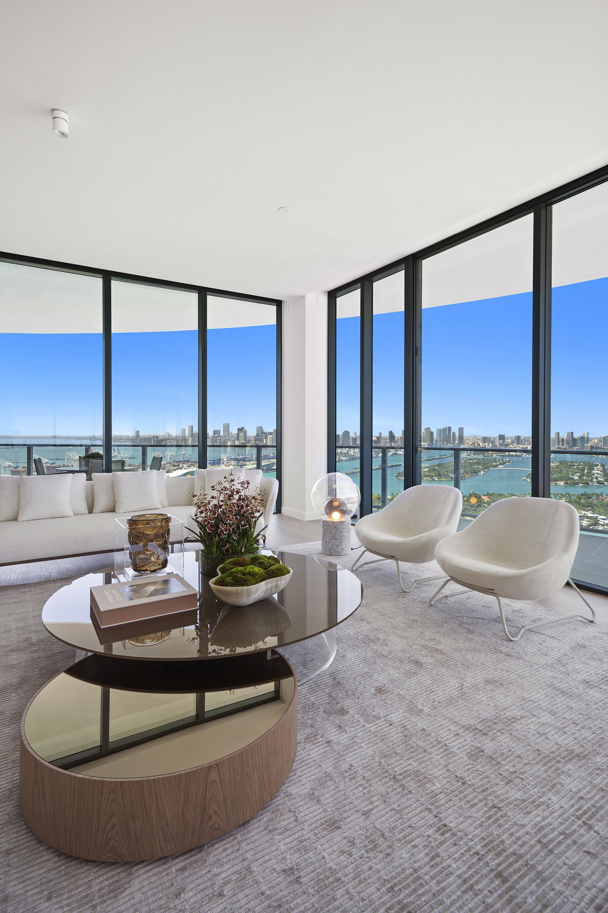 Modern living room with large windows, white furniture, and a view of the city skyline.