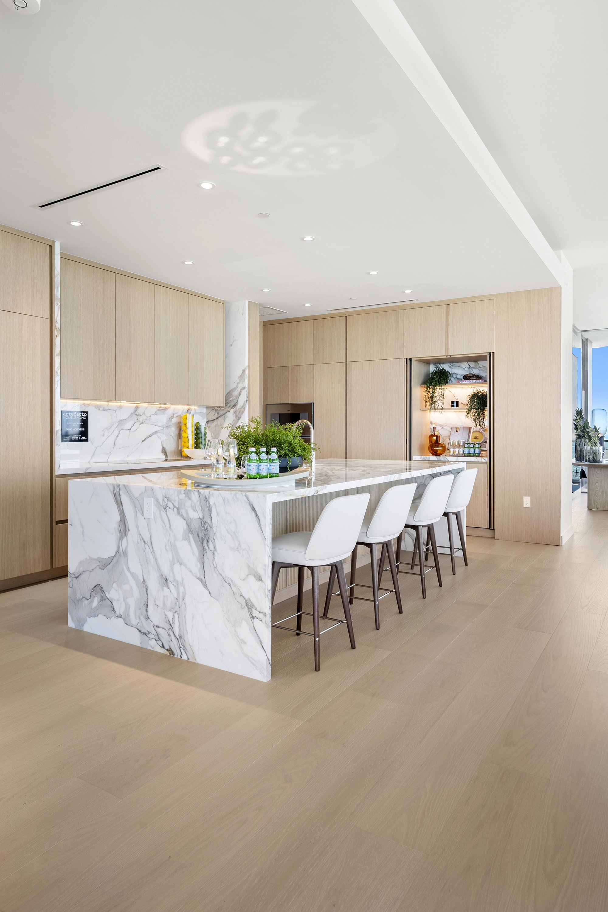 Modern kitchen with marble island, wooden cabinets, and white barstools.