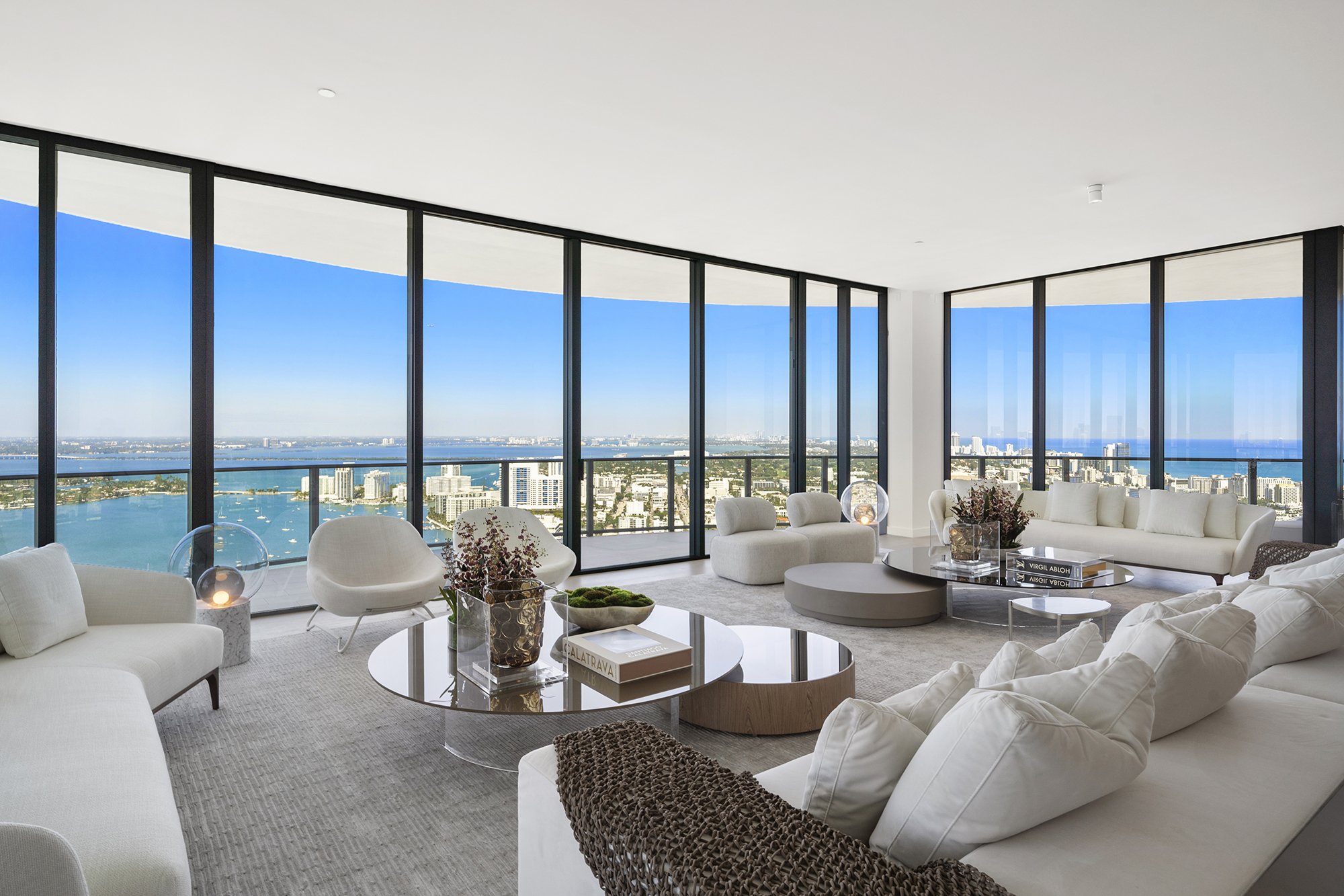 Modern living room with large windows, city and ocean view, white sofas, and glass coffee tables.