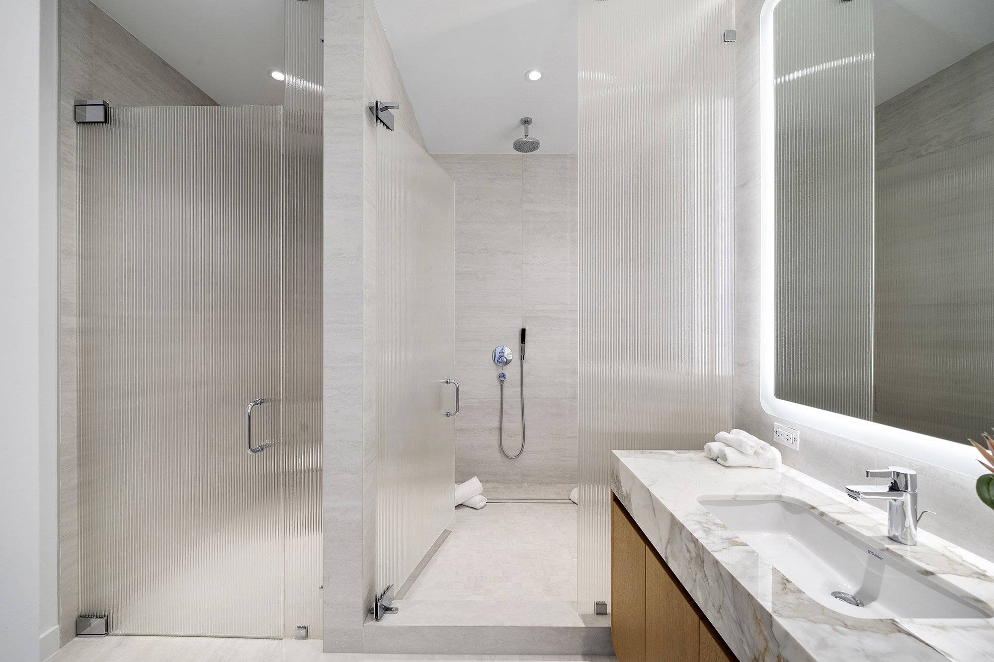 Modern bathroom with glass shower enclosure, marble countertop with sink, wall-mounted mirror, and towels.