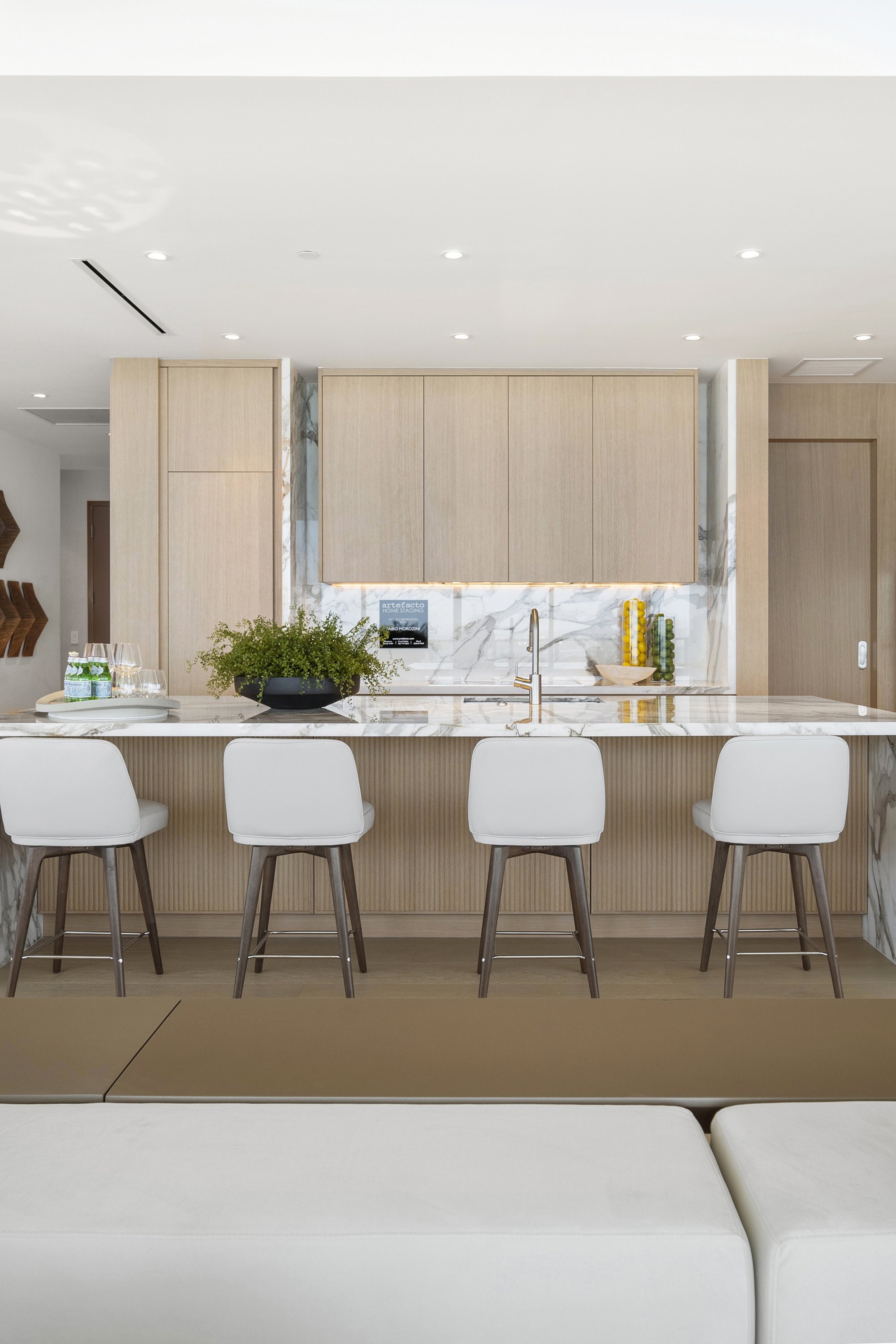 Modern kitchen with marble countertop, wooden cabinets, and four white bar stools.