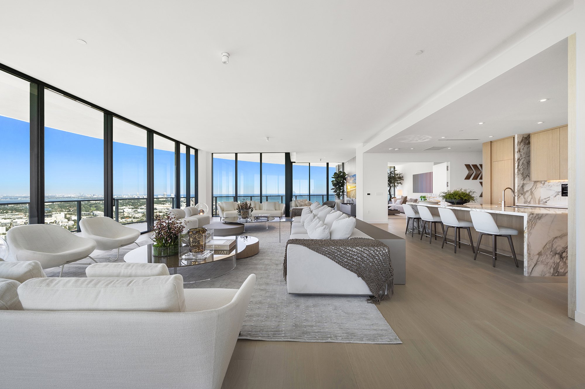 Spacious modern living room with large windows, white sofas, and open kitchen with marble countertops.