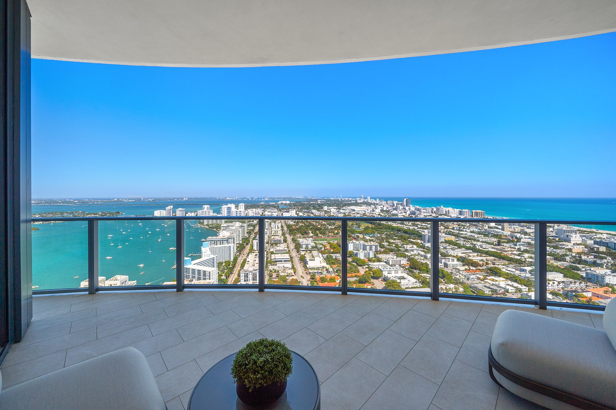 Ocean view from high-rise balcony with glass railing, overlooking cityscape and boats on the water.