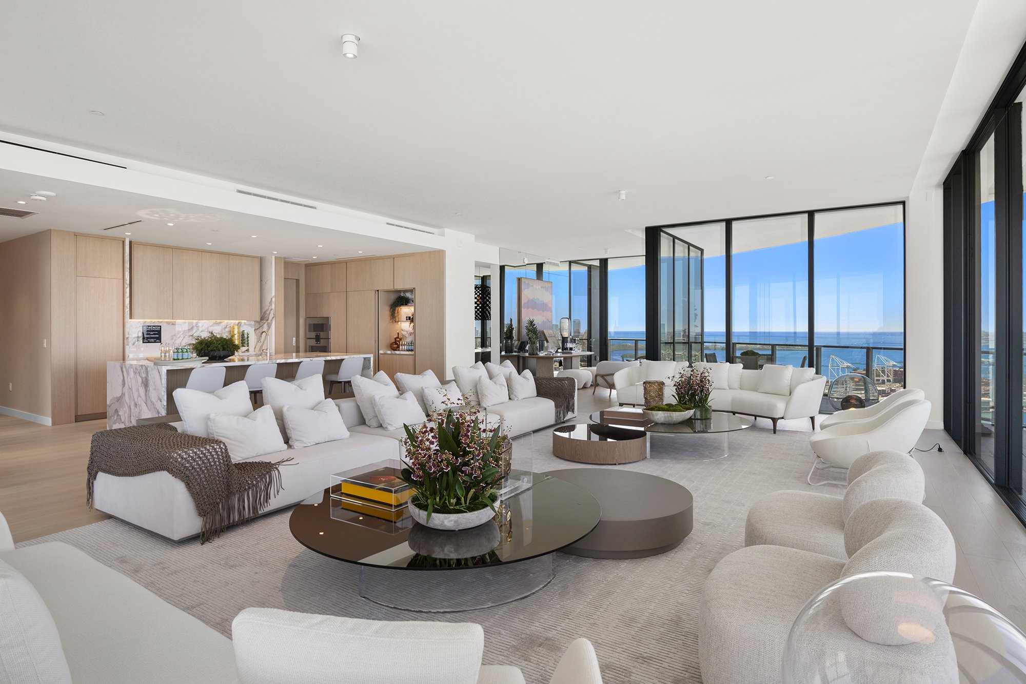 Luxurious modern living room with large windows, ocean view, white sofas, round coffee tables, and contemporary decor.
