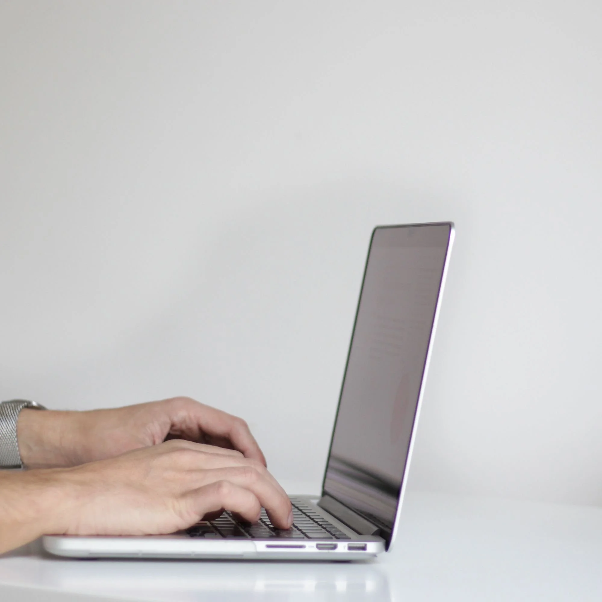 Person typing on a silver laptop with a minimalist white background.