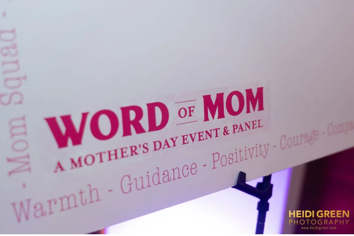 Sign for a Mother's Day event titled 'Word of Mom' with words like warmth, guidance, positivity, courage, compassion, and honesty at the bottom, including a photo credit to Heidi Green Photography.