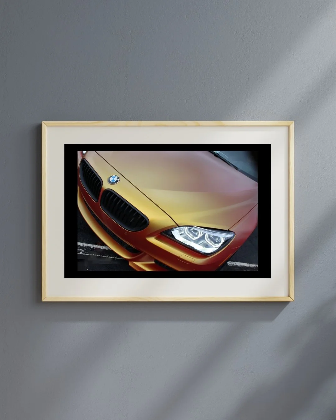 Framed photo of a gold BMW with headlight detail on a gray wall.
