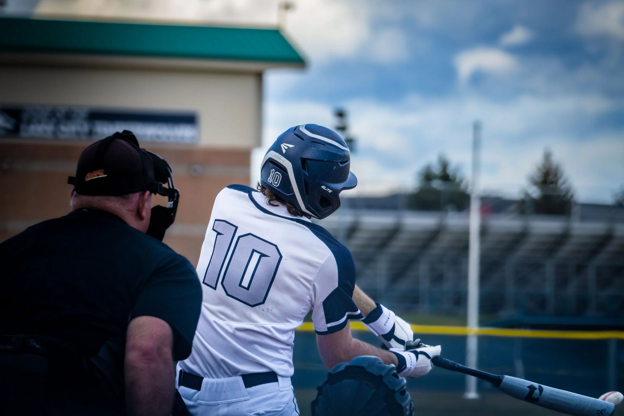Baseball batter swinging the bat during a game, with an umpire behind, wearing a helmet and jersey number 10, outdoor stadium setting.