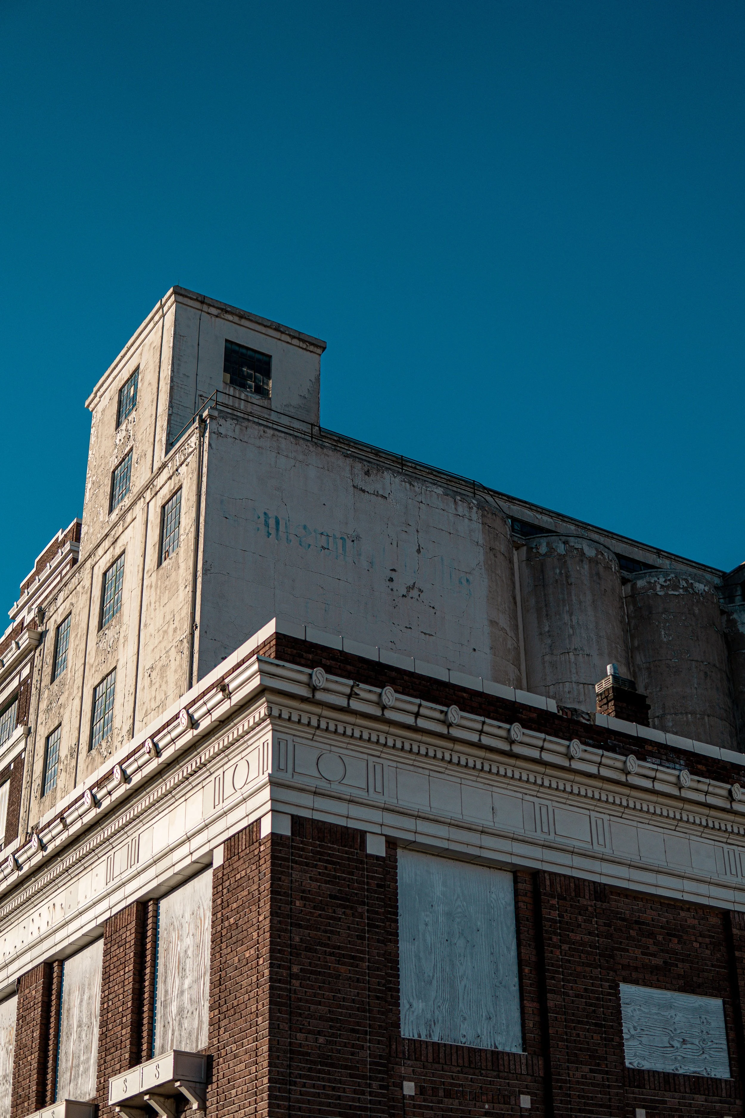 Old abandoned brick building with faded signs and boarded windows under a clear blue sky.