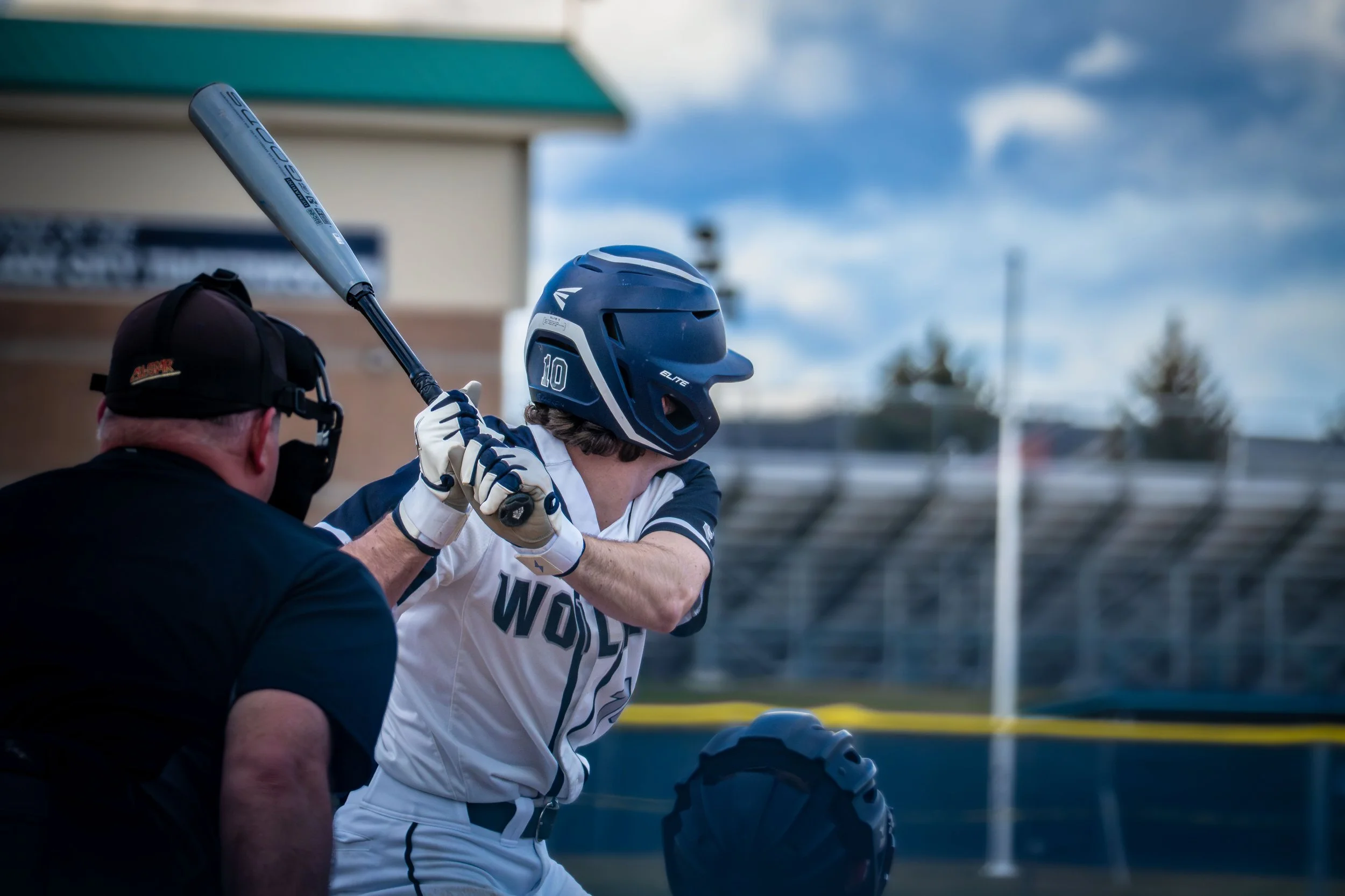 Baseball player at bat ready to hit during a game, wearing a helmet and uniform. An umpire and catcher are in position behind the player.