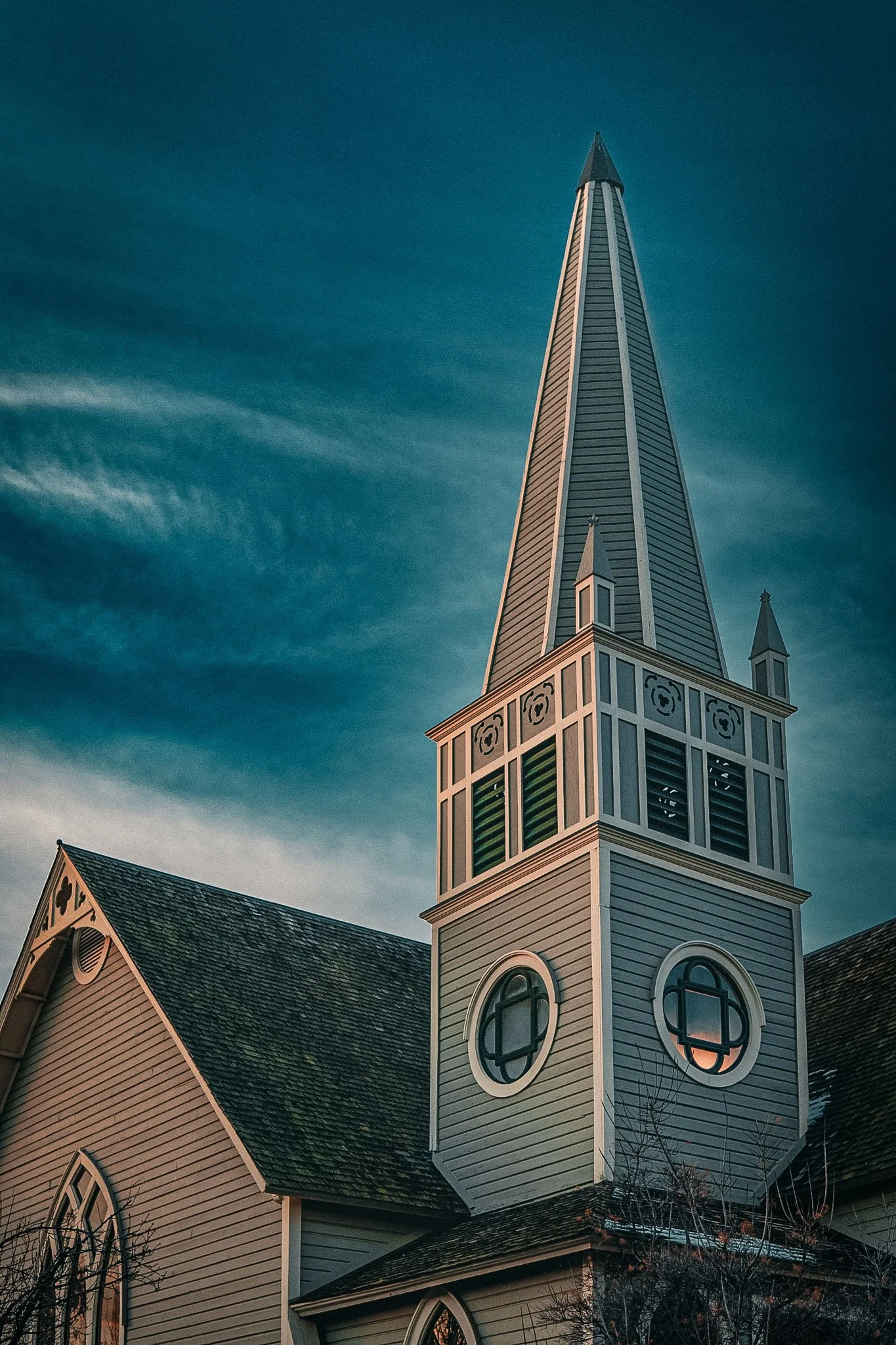 Church steeple under a cloudy sky with ornate windows and wooden exterior.