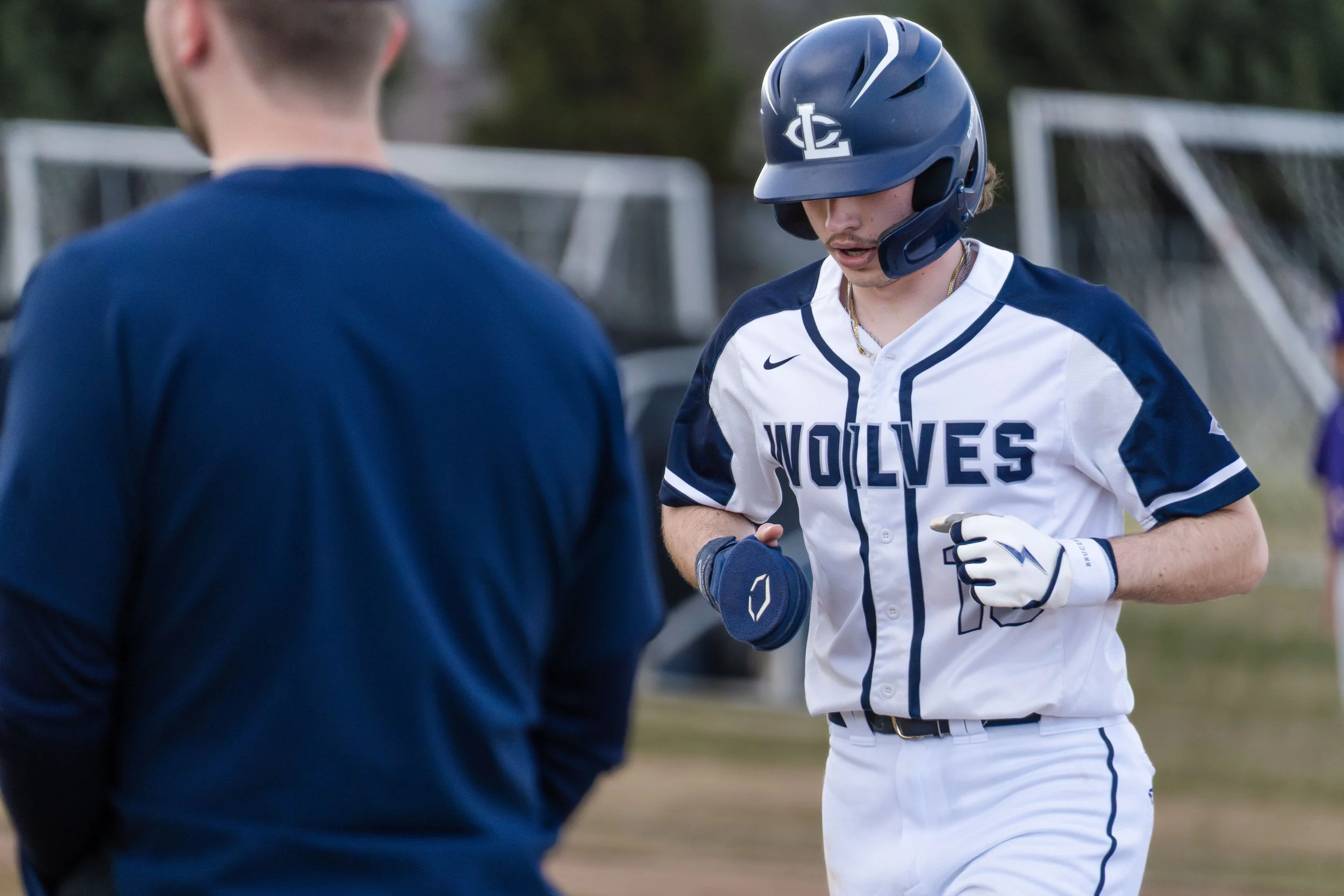 Baseball player in Wolves uniform and helmet jogging on field with another person in blue shirt.