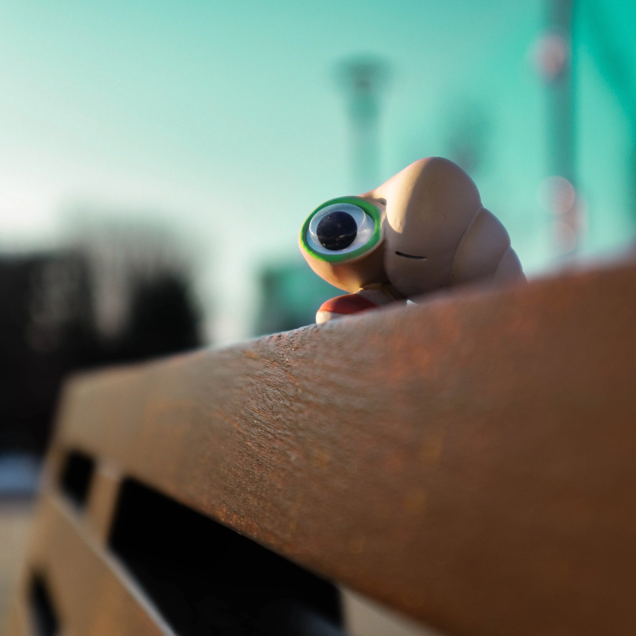Close-up view of a small toy figure of Marcel The Shell with Shoes On, partially visible, with a turquoise background and some out-of-focus objects in the foreground.