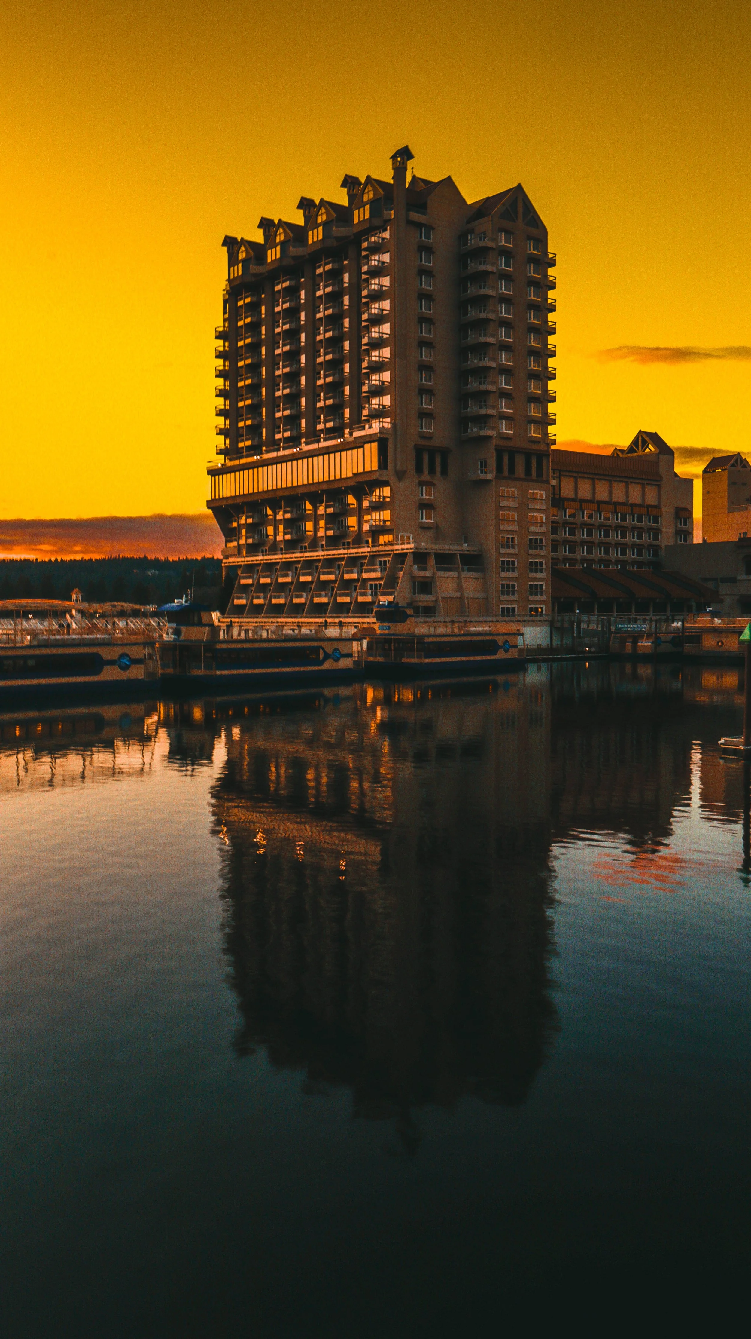 The Coeur d'Alene Resort is reflected on the water below during sunset, with a yellow-orange sky in the background.