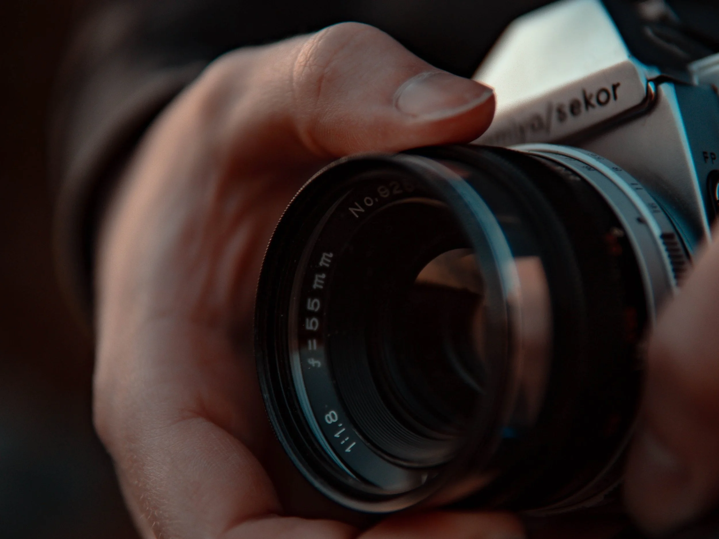 Close-up of a person's hand adjusting the focus ring on a black camera lens.