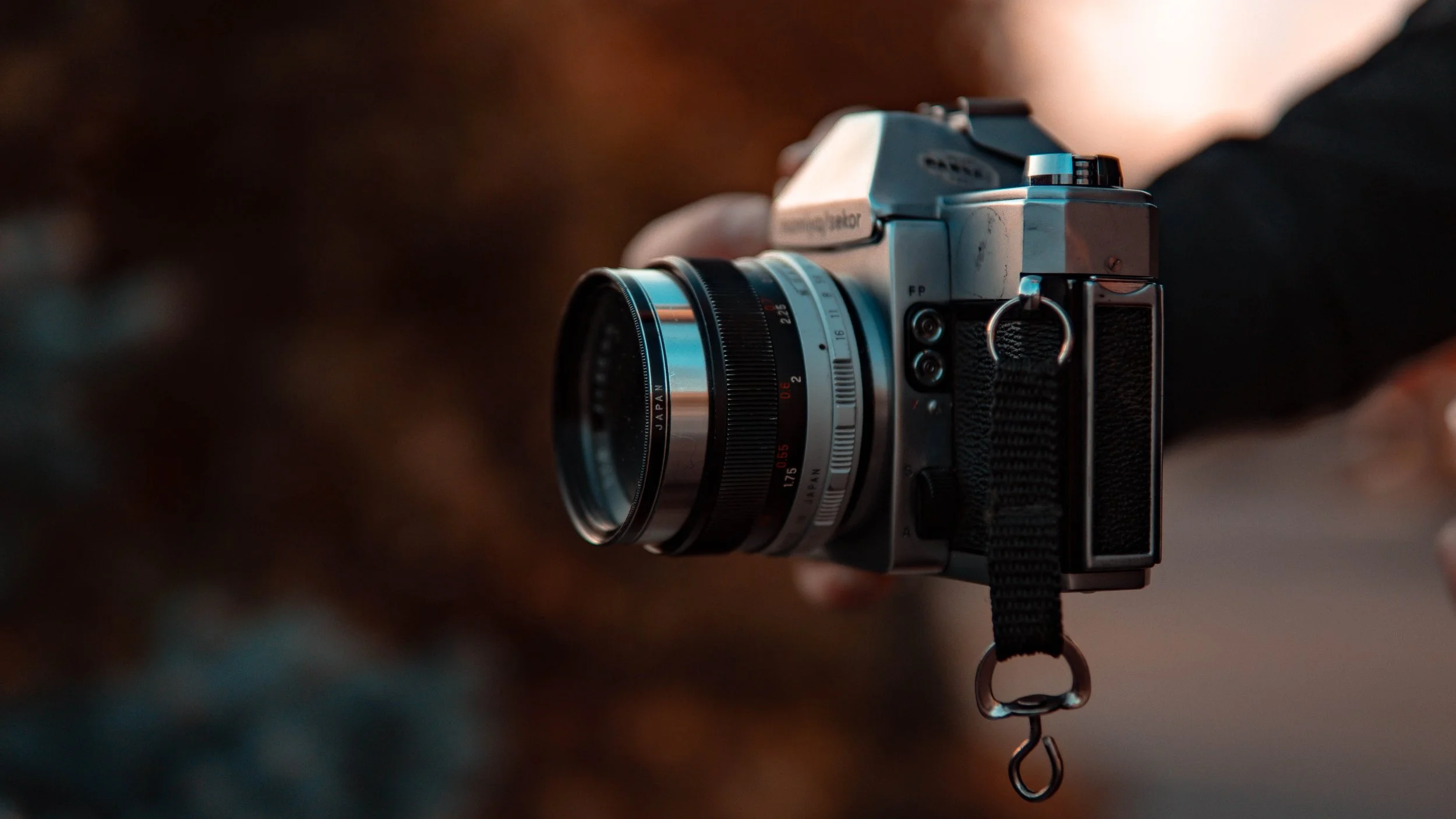 Close-up of a vintage camera with a zoom lens, held by a person with a blurred background.