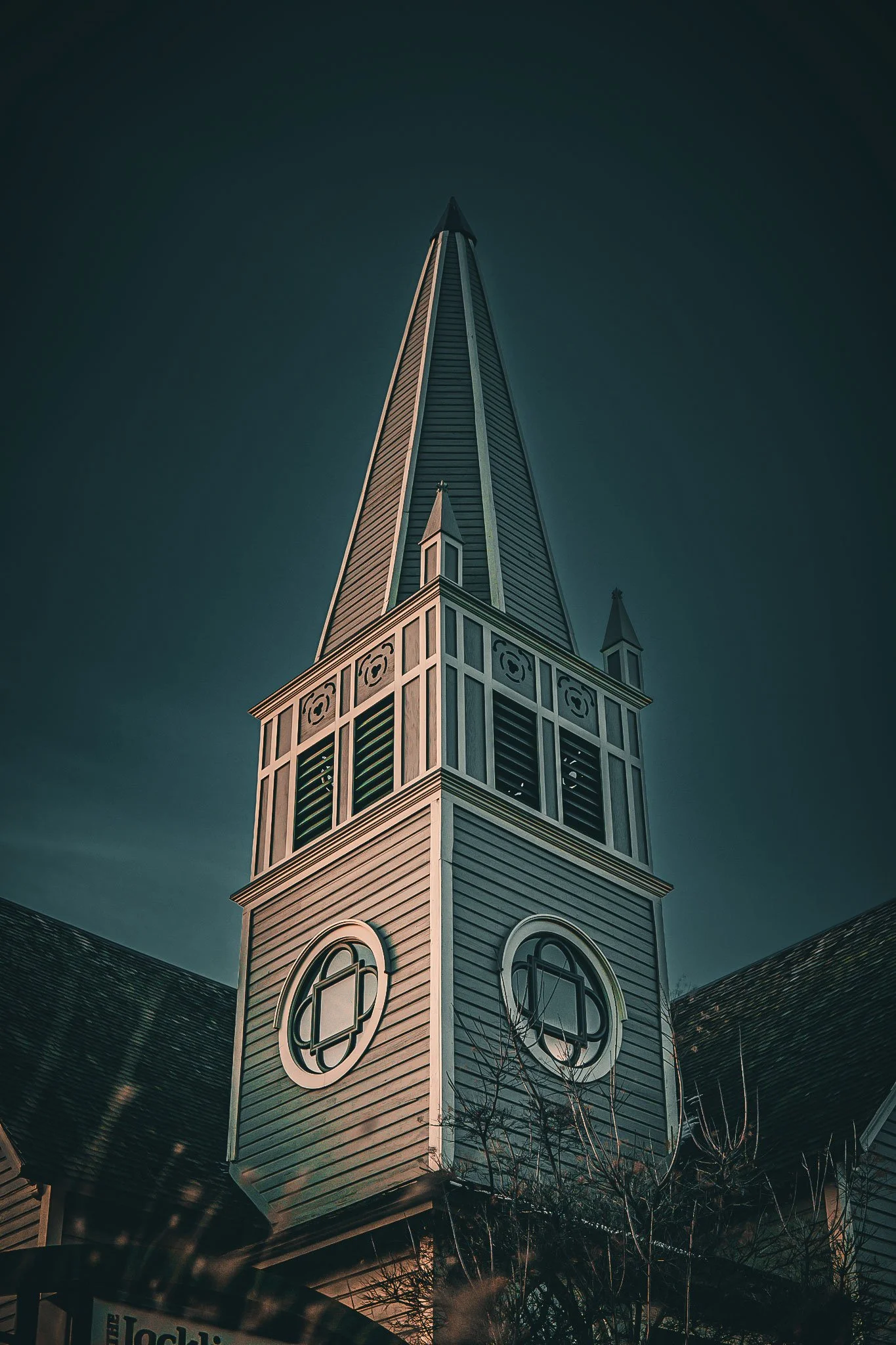 A church steeple with a pointed roof and circular windows against a dark sky.
