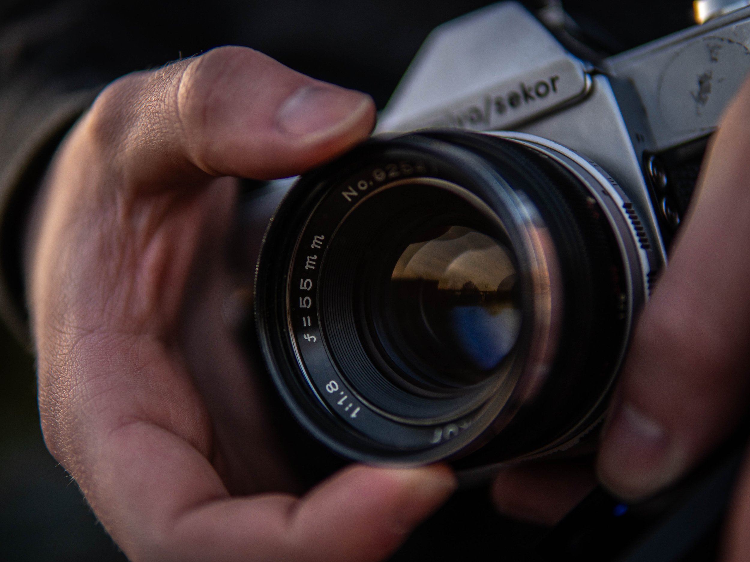 A close-up of a person's hand holding a vintage camera, with focus on the camera's lens.