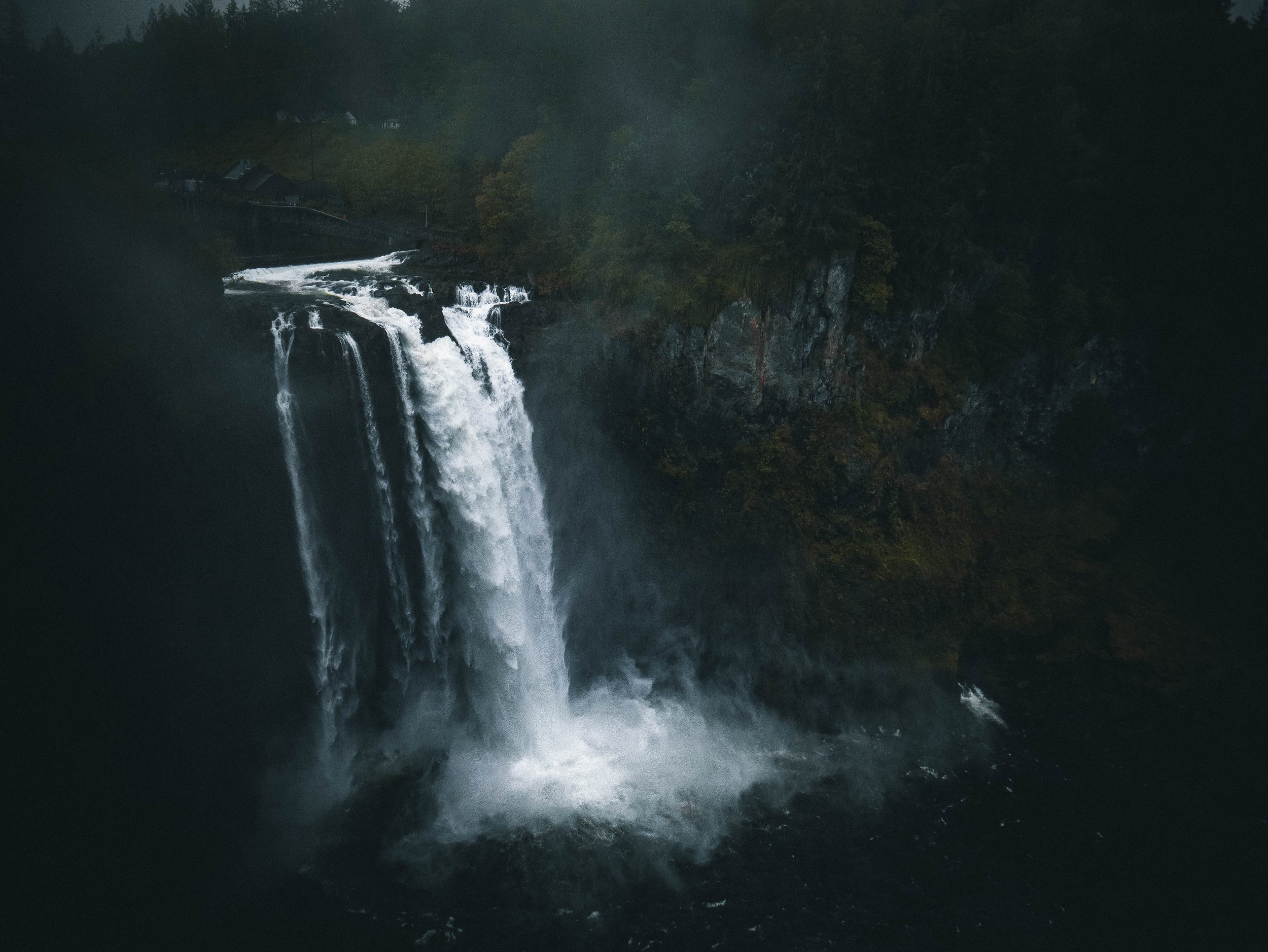 A waterfall cascading over rocks in a forested area with trees and fog in the background.