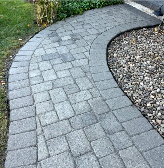 Curved pathway made of gray pavers next to a garden bed filled with smooth, rounded stones.