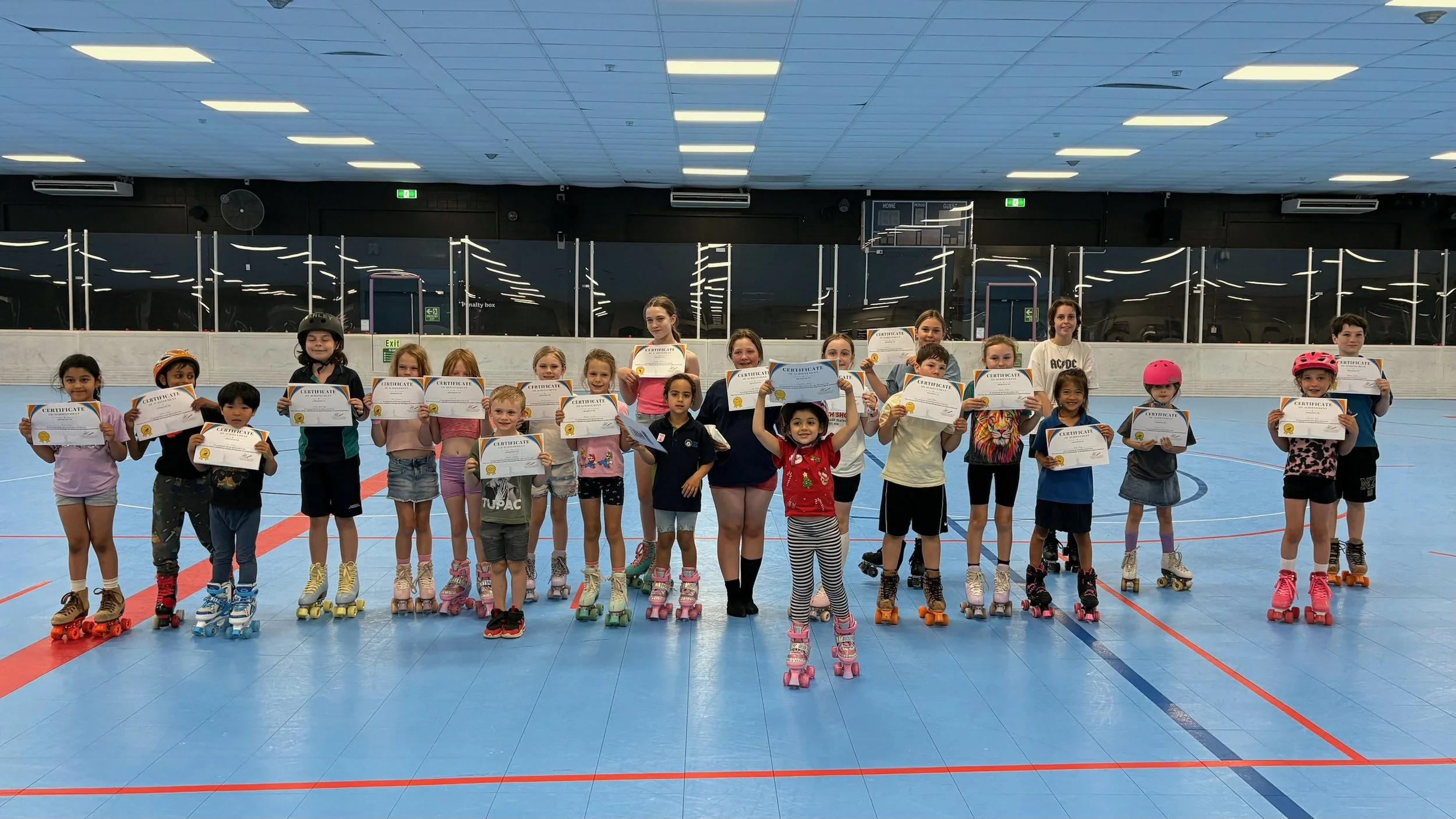 Group of children in roller skates holding certificates at an indoor roller skating rink.