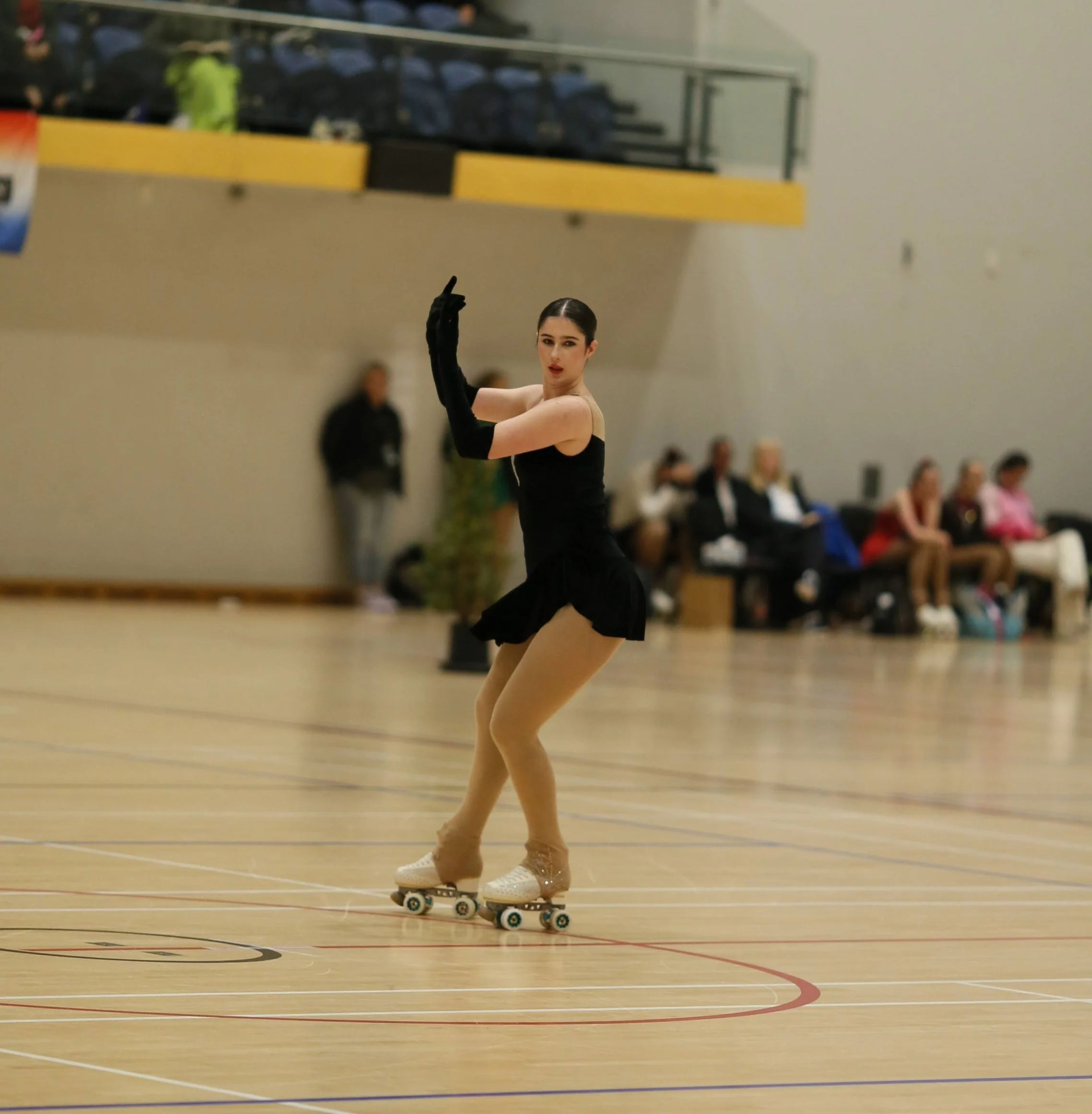 female roller skater in a black dress performing a move on a wooden roller skating rink