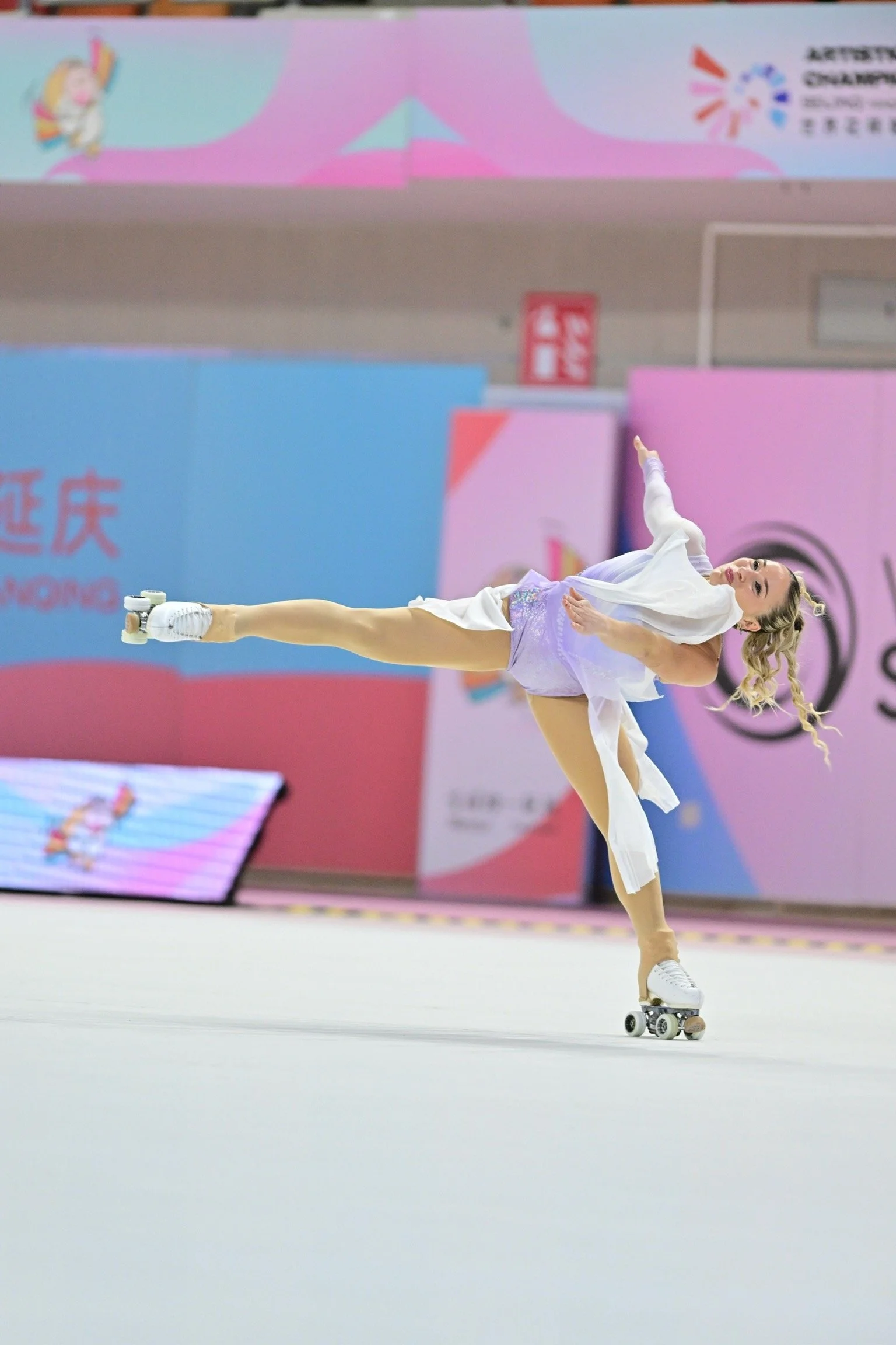 A female figure skater performing a move on roller skates during a competition.