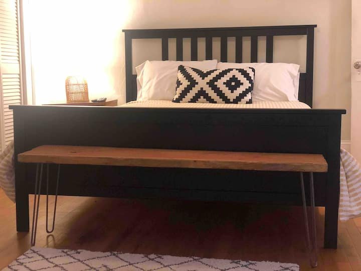 Bedroom with black wooden bed frame, decorative pillow, bench, and soft lighting.