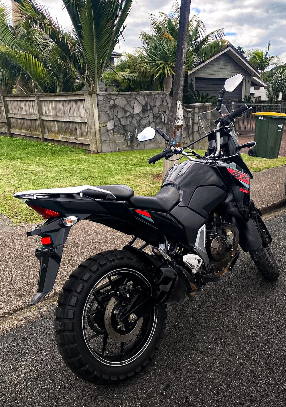 Motorcycle parked in a residential area with palm trees and houses in the background.