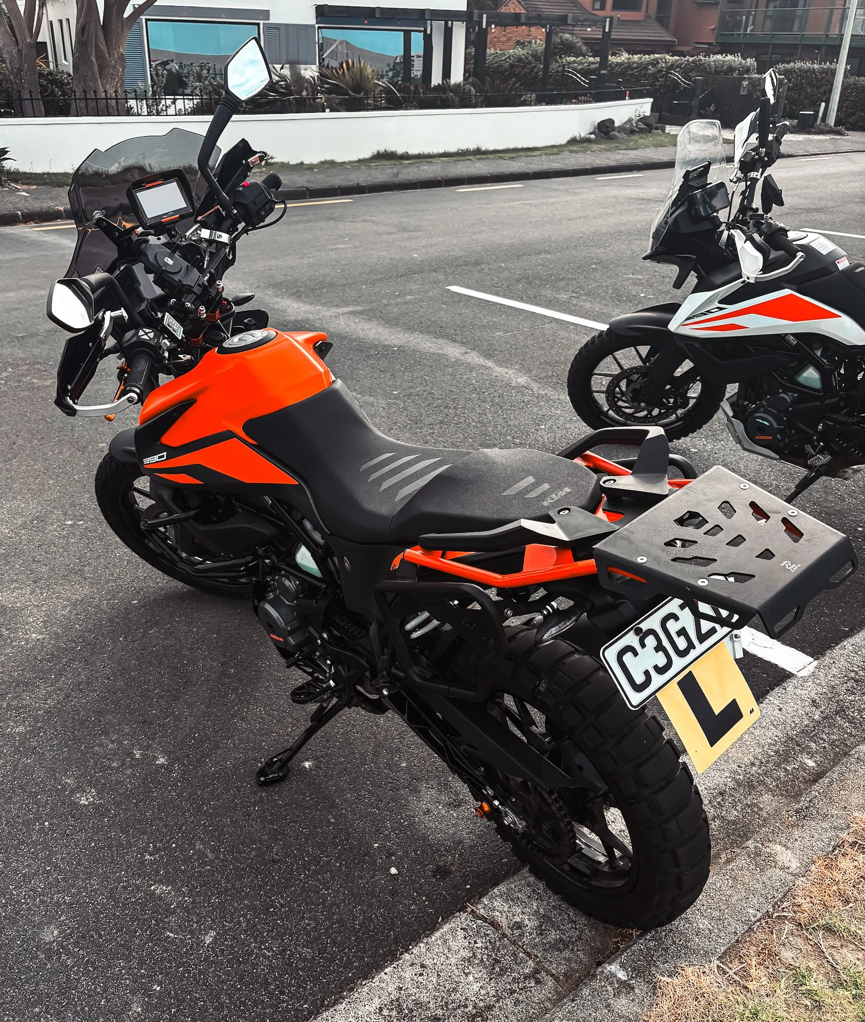 Orange and black motorcycle parked on a street with a yellow learner's plate, alongside another motorcycle.