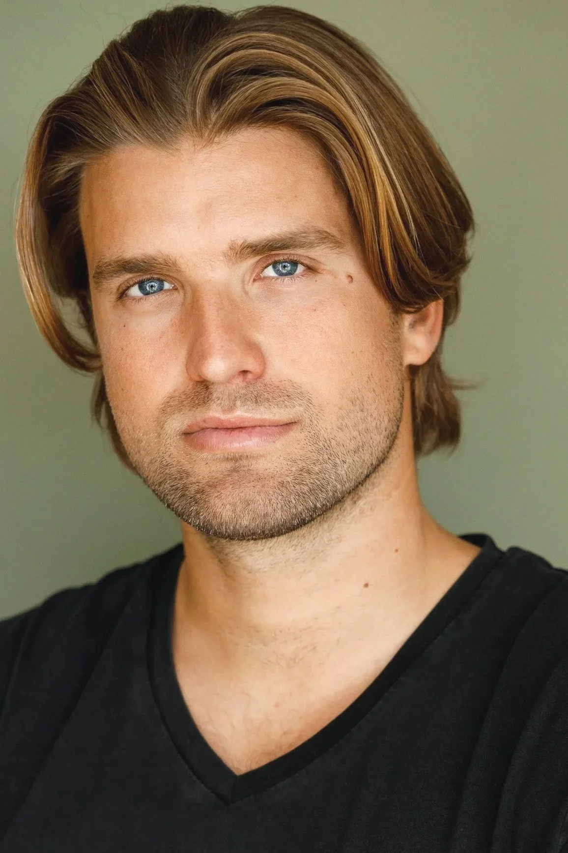Portrait of a man with long hair and a black shirt, looking directly at the camera with a neutral expression.