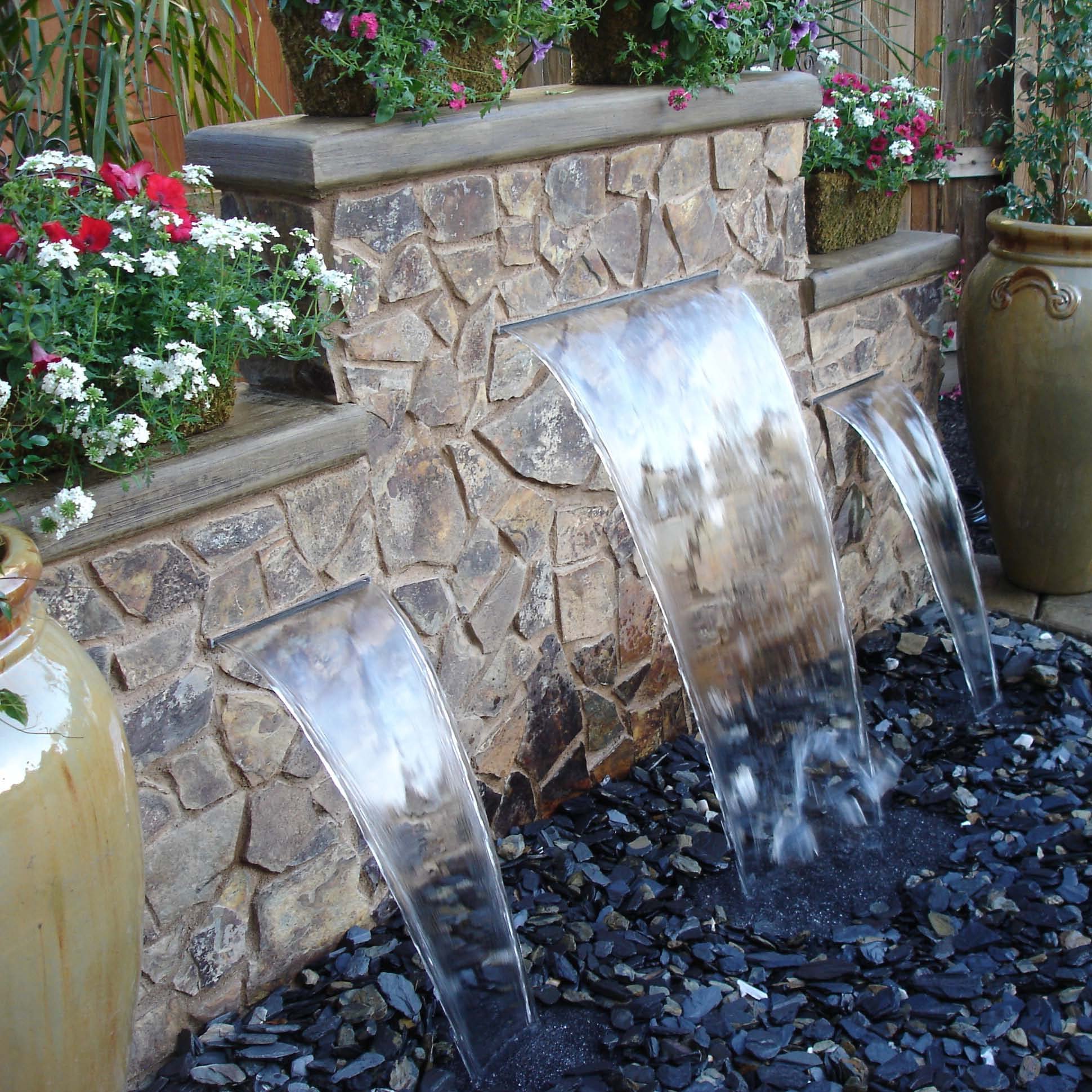 Stone outdoor water feature with cascading waterfalls and surrounding flowers.