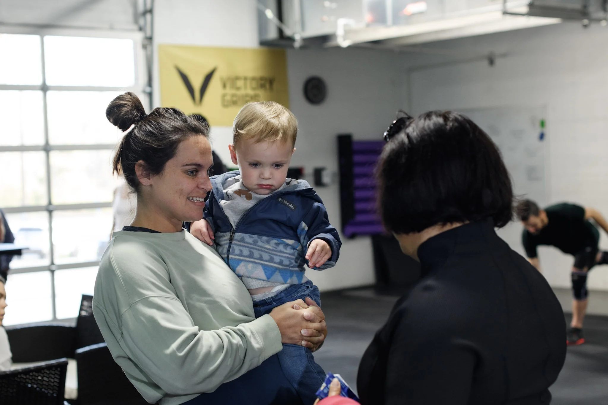 A mom holding her toddler on the gym floor at Coefficient CrossFit