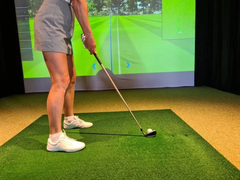 Person preparing to hit a golf ball in a virtual golf simulation room.